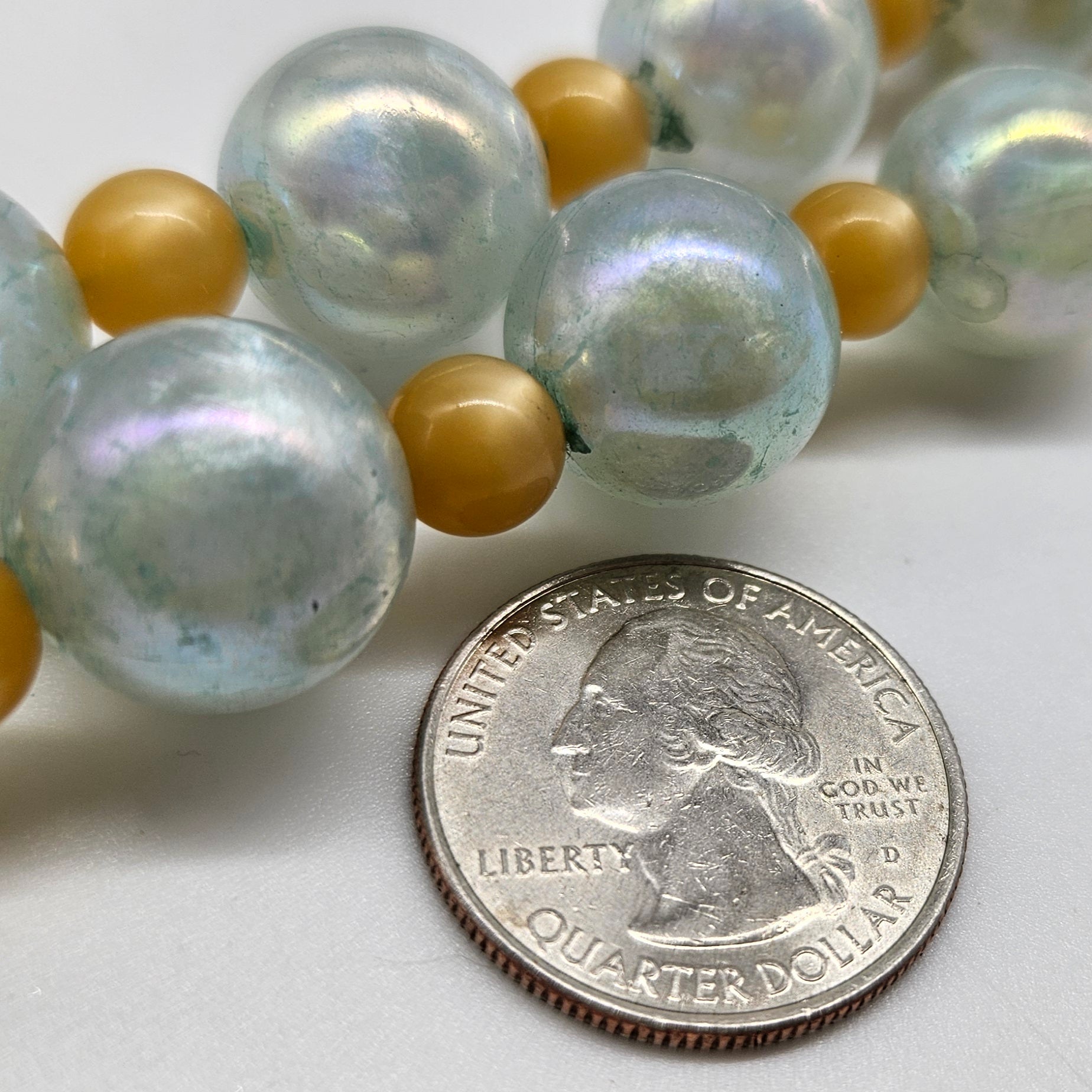 Close-up of a necklace with large beads next to a U.S. quarter dollar coin on a white background