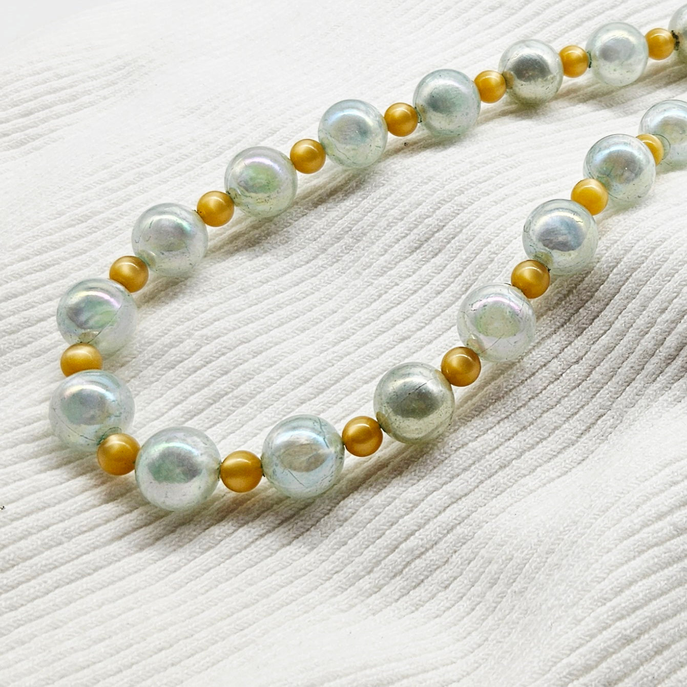 Pearlized and golden bead necklace on a textured white surface