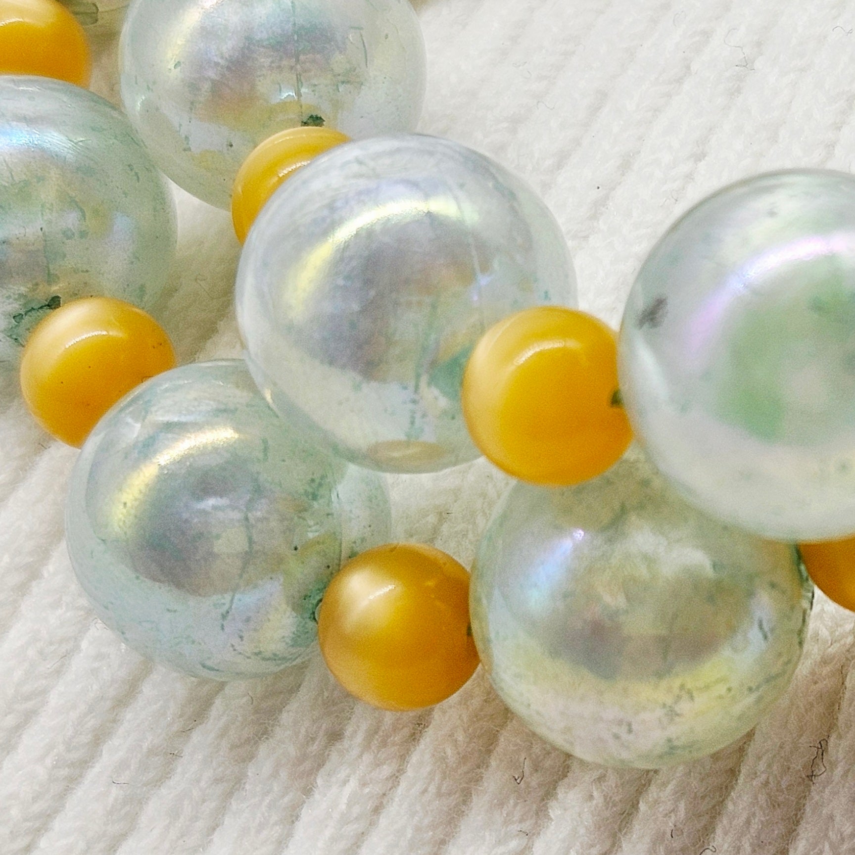 Close-up of a necklace with large pearlized beads and smaller golden yellow spacers on a textured white background