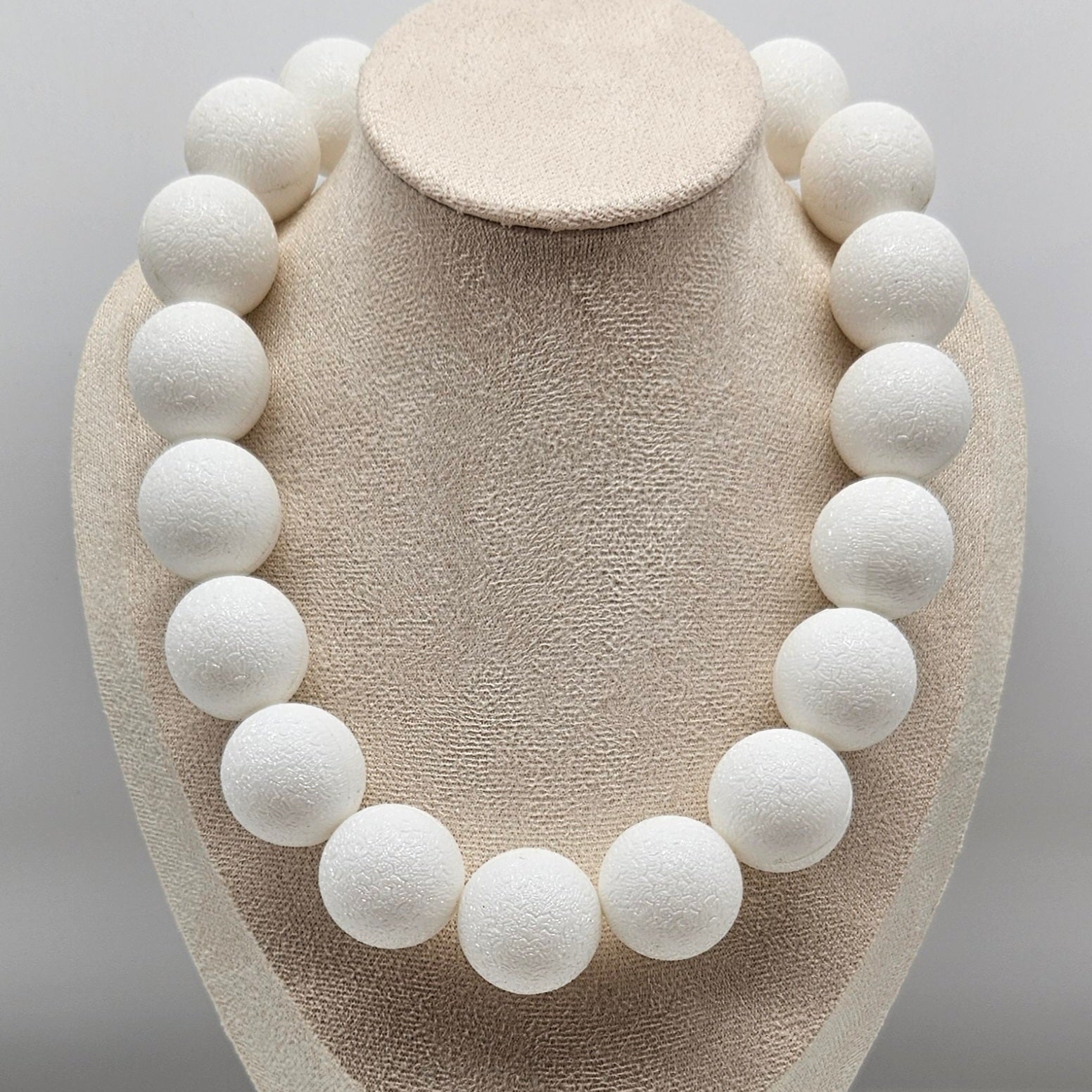 White spherical necklace on a beige mannequin bust against a gray background