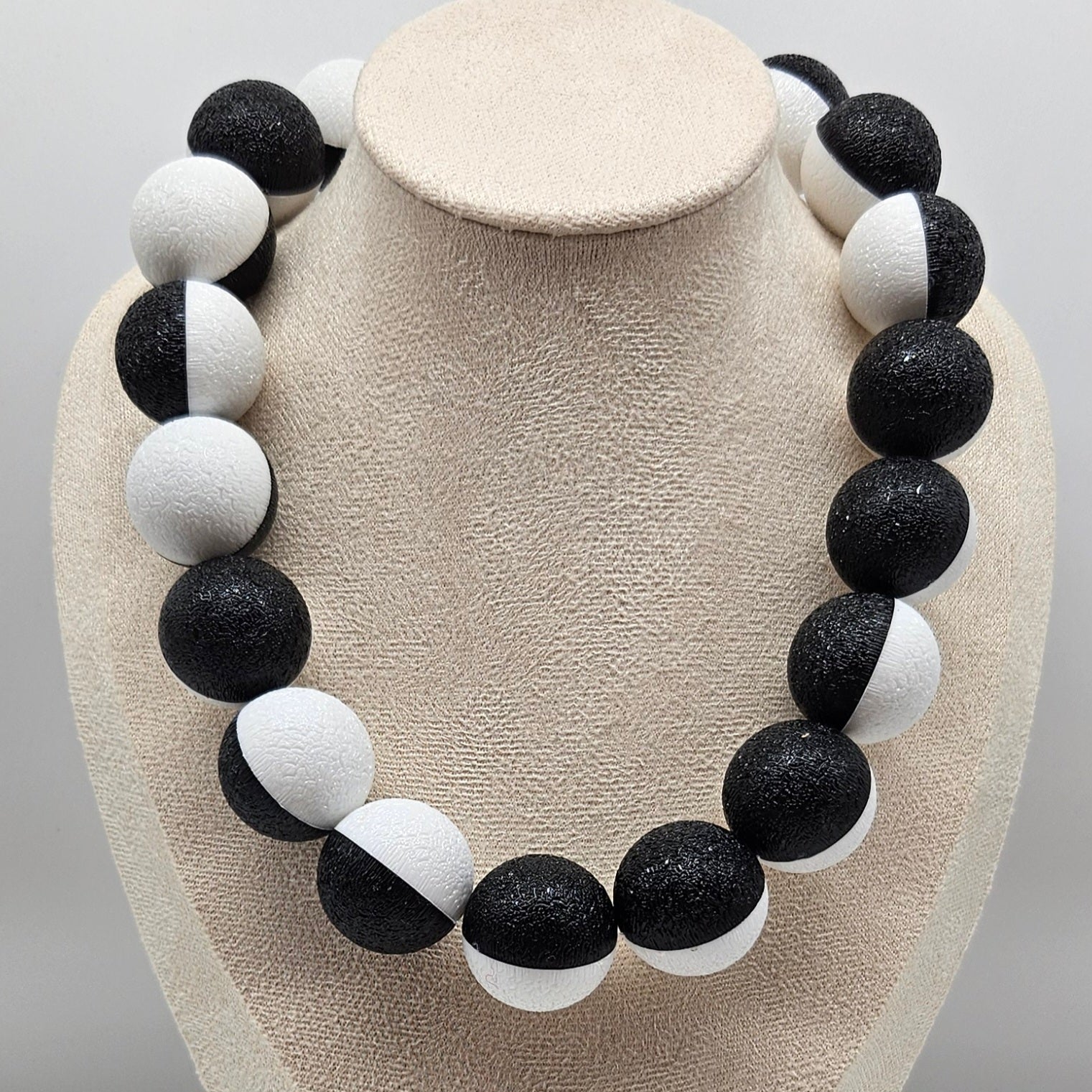 Necklace with black and white beads on a beige display stand.