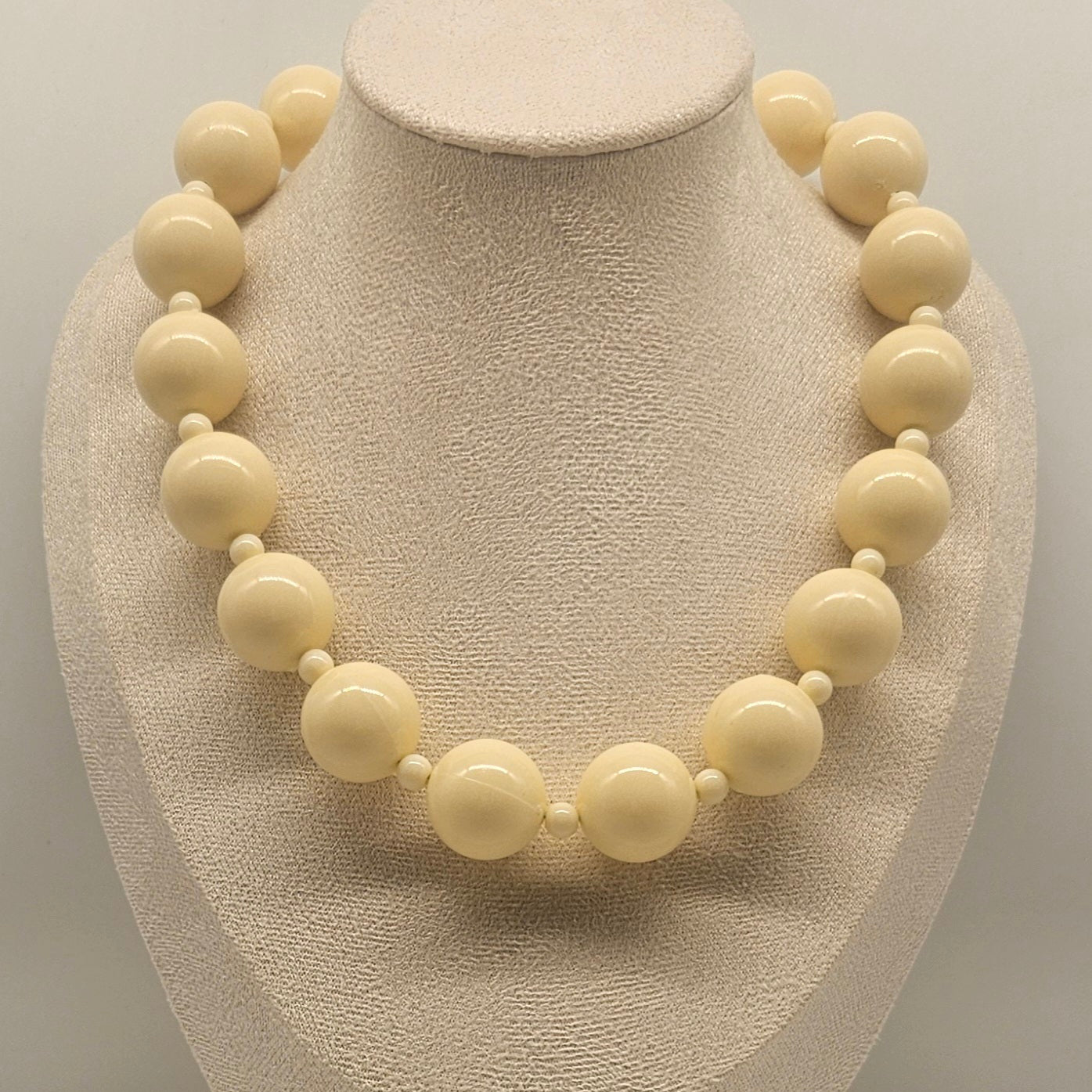Necklace with large cream-colored beads on a mannequin bust against a neutral background