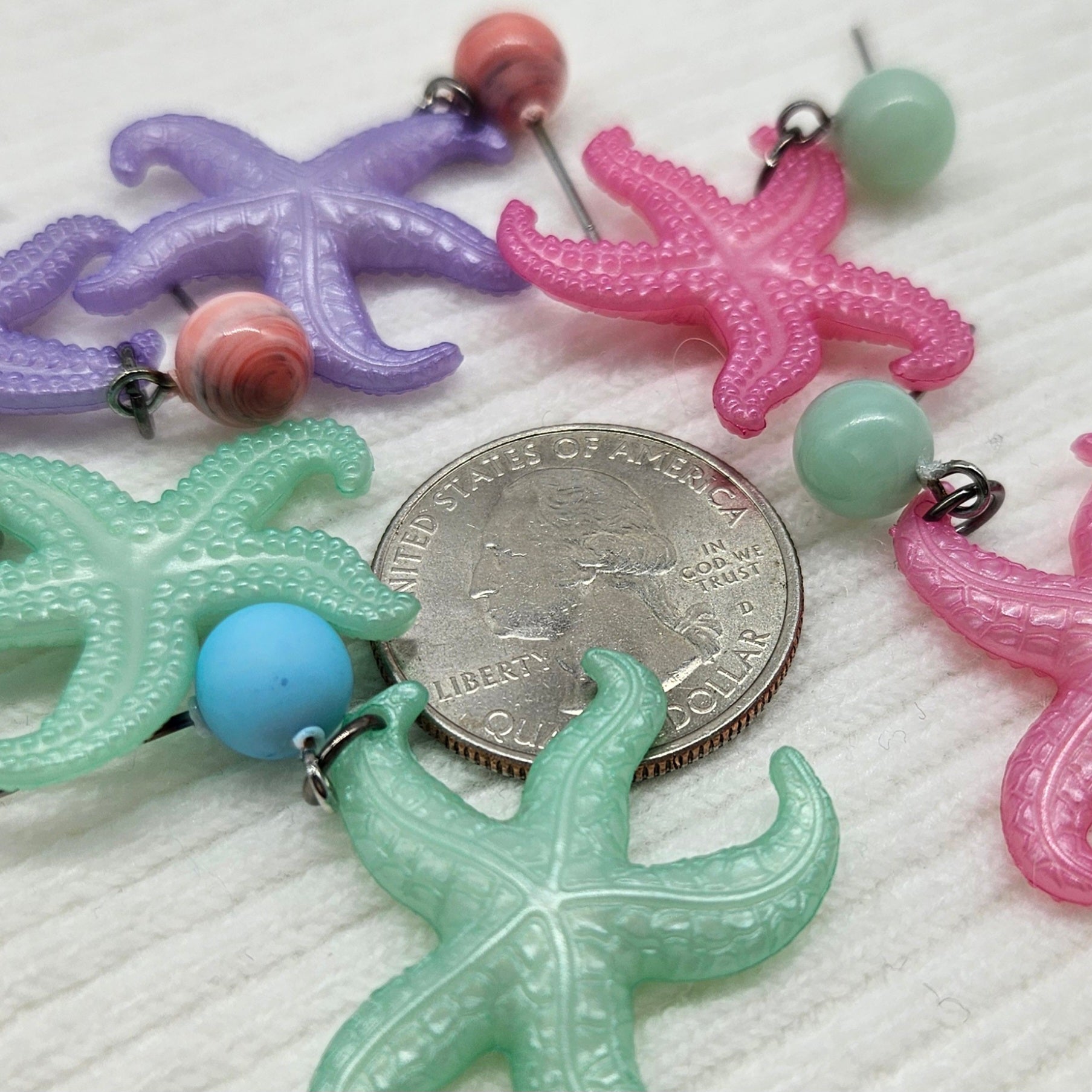 Colorful starfish-shaped earrings with a US Quarter for scale on a white surface.