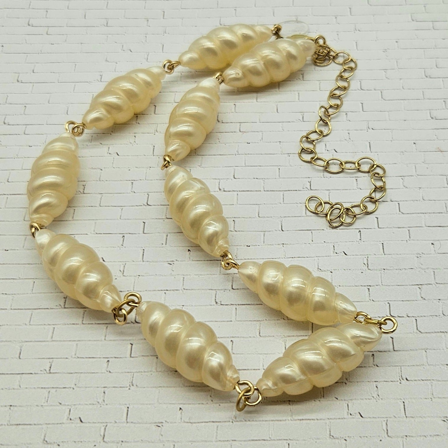Lucite pearl necklace with gold chain on a textured white background
