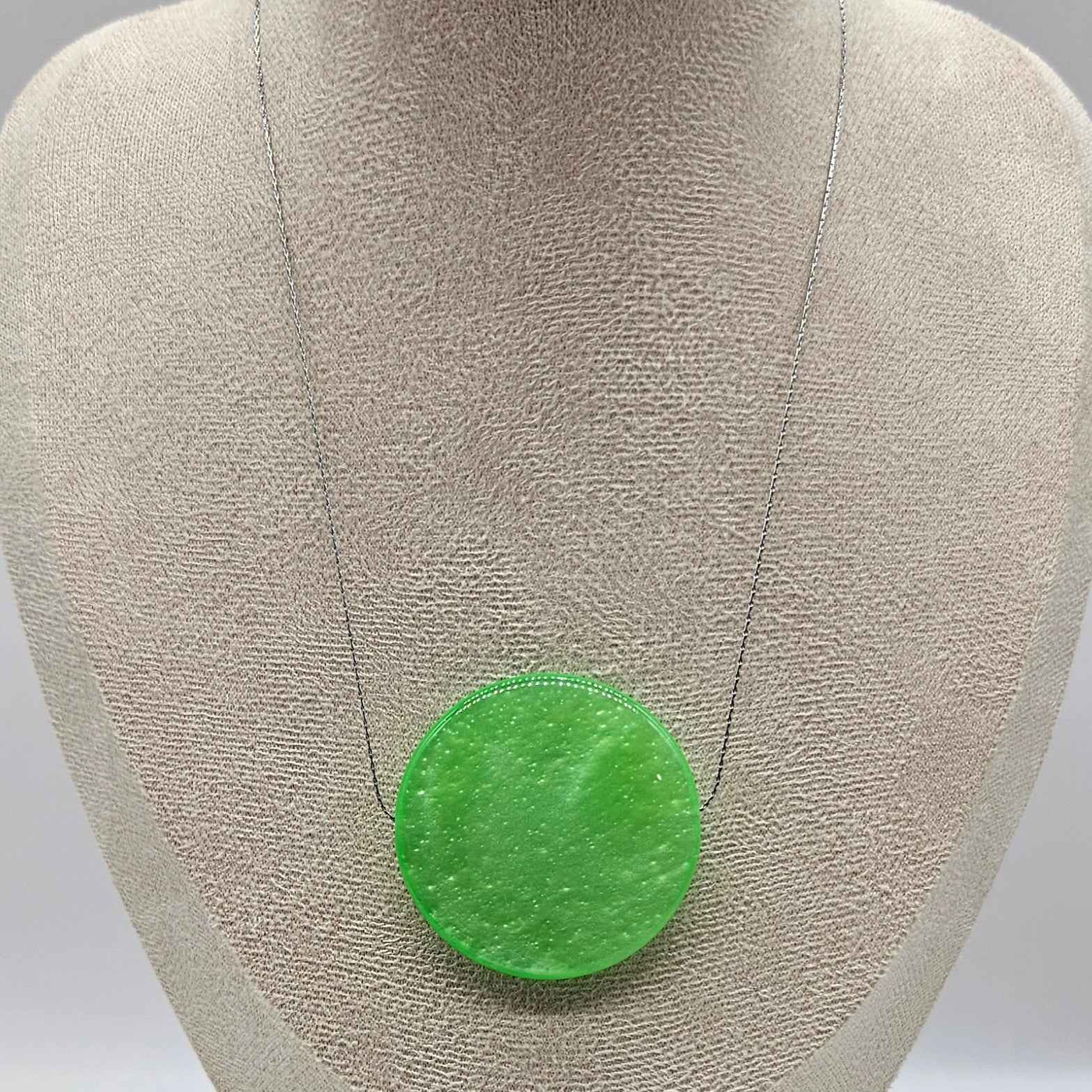 Green circular pendant on a gray fabric background