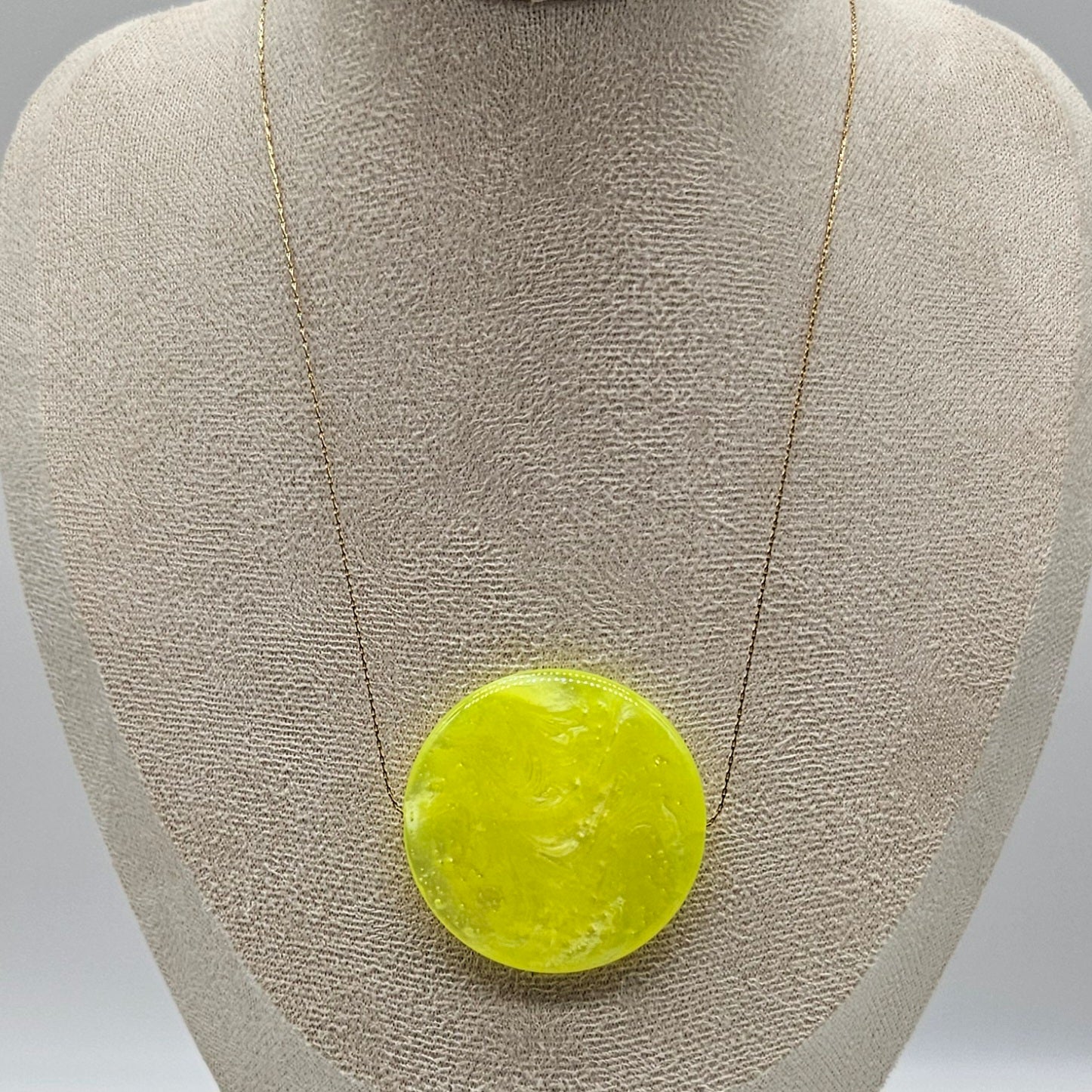 Necklace with a round, yellow pendant on a gray bust