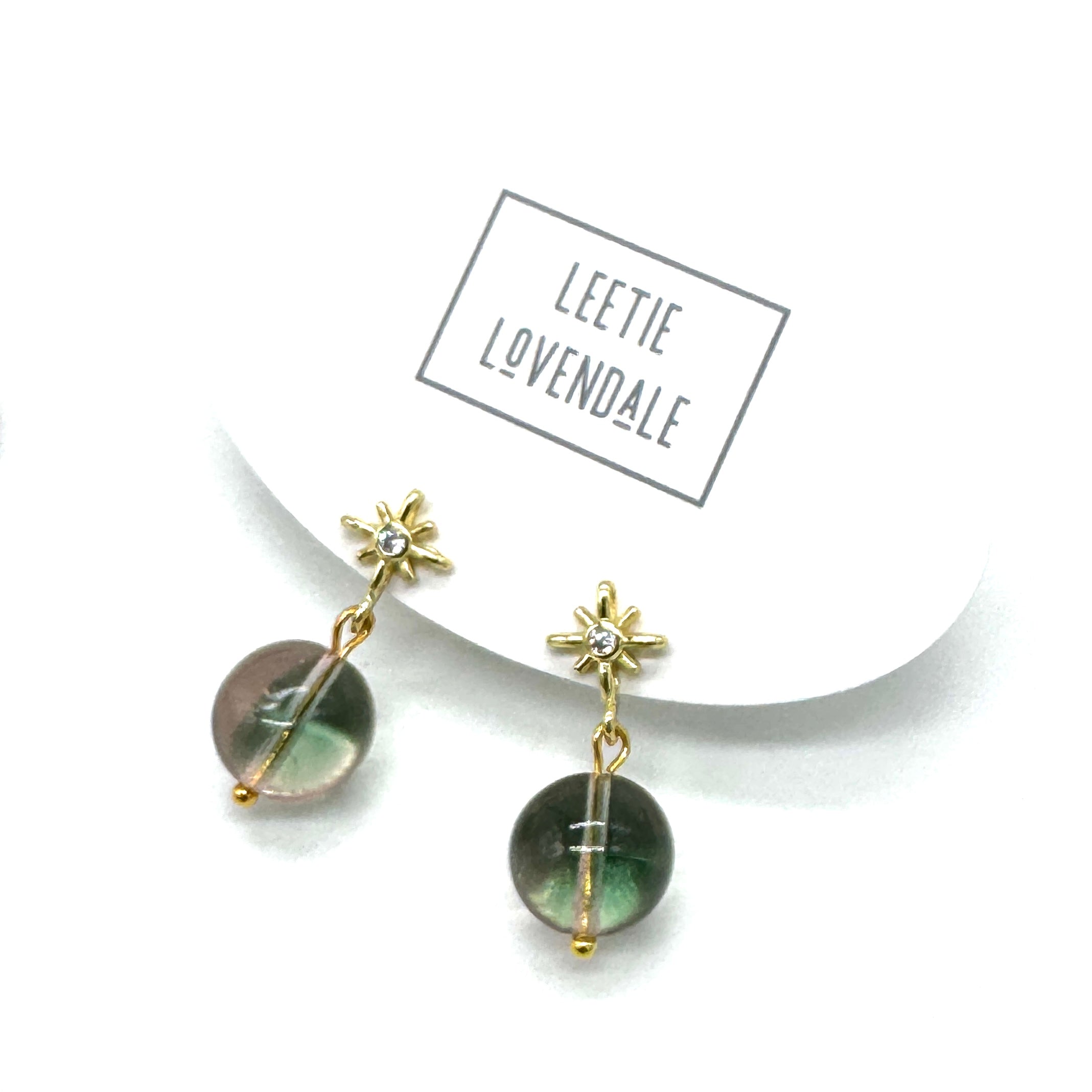 Gold earrings with green stones on a white background with &