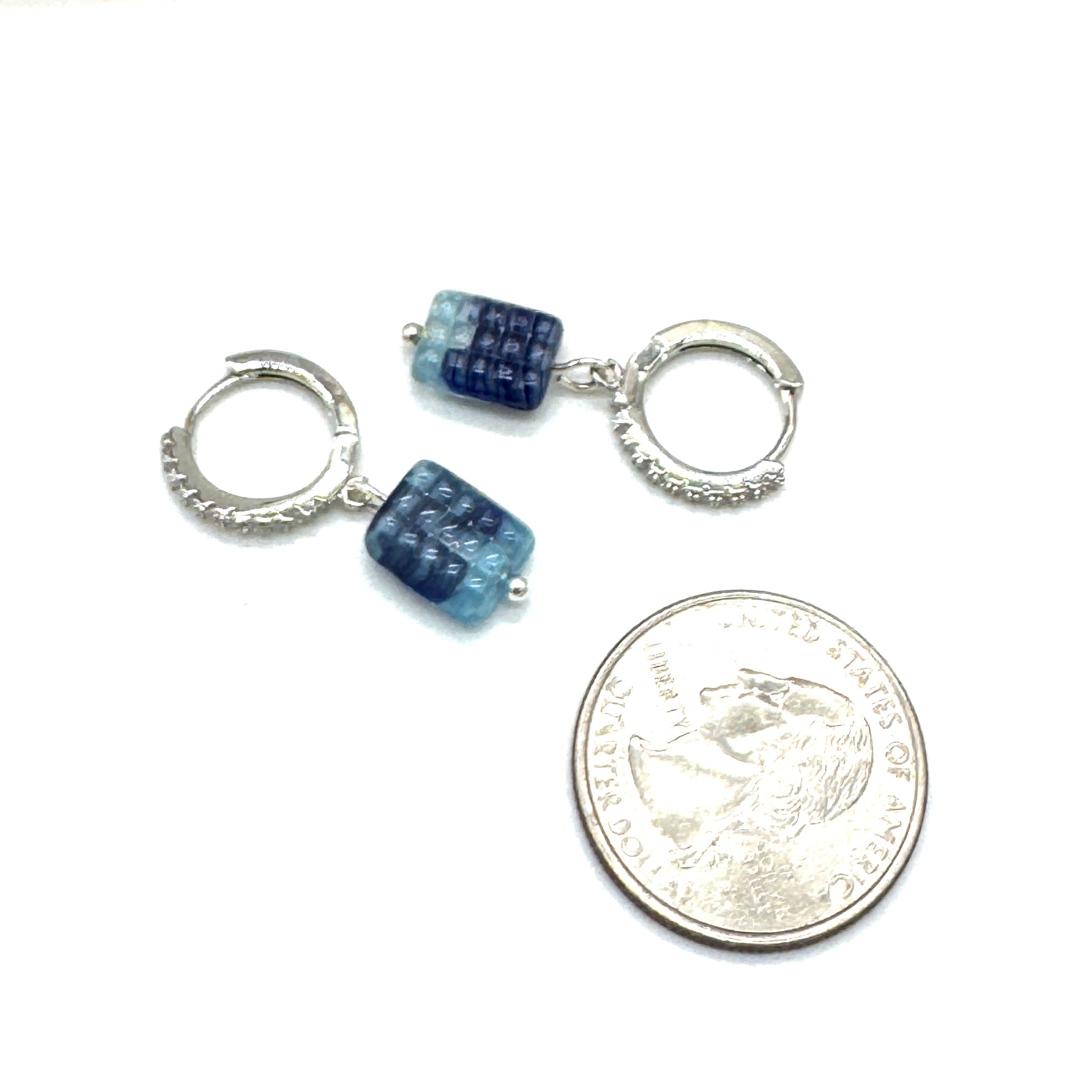 Pair of silver hoop earrings with blue gemstones next to a quarter for scale on a white background