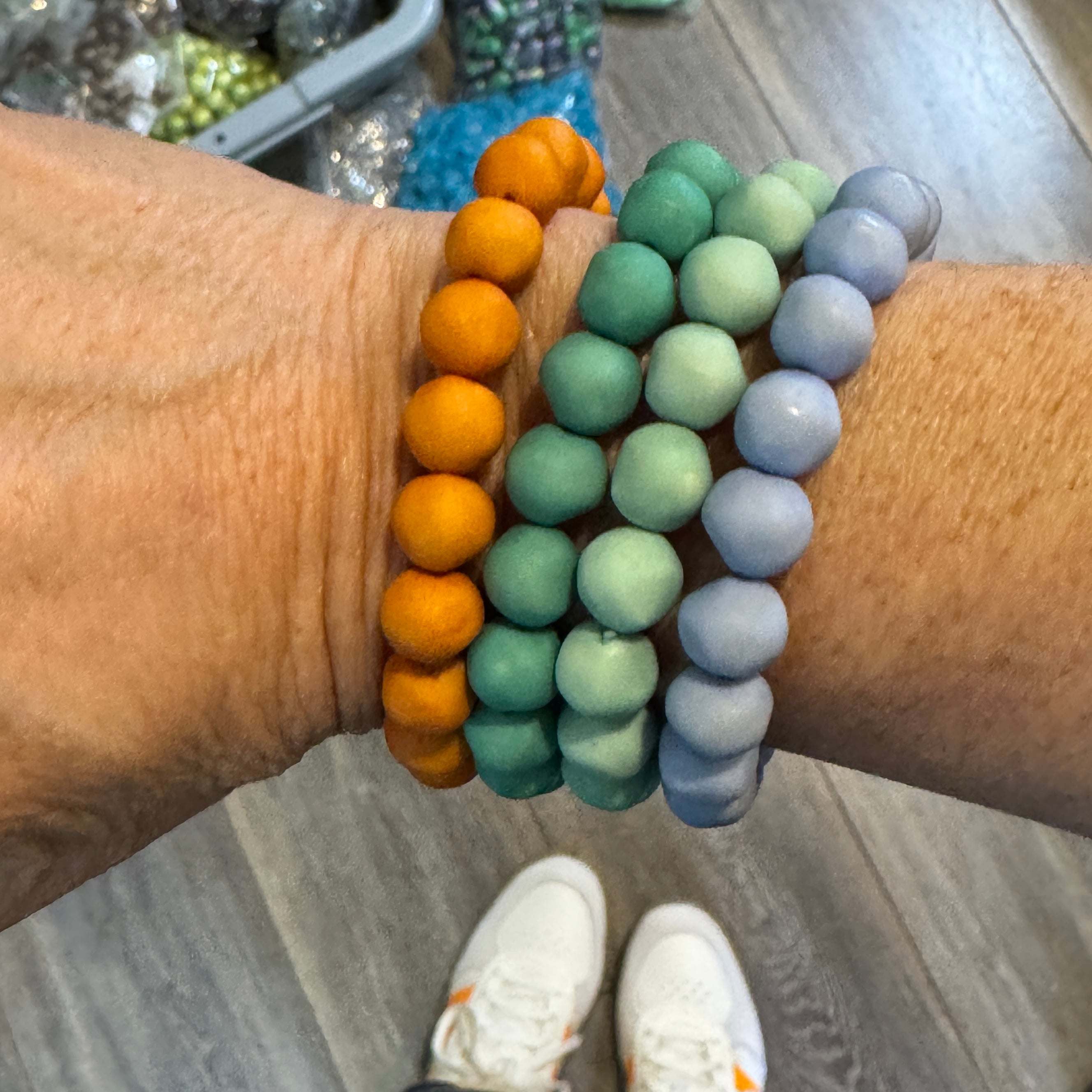 Set of four lucite beaded bracelets in orange, teal, turquoise, and periwinkle worn on a wrist