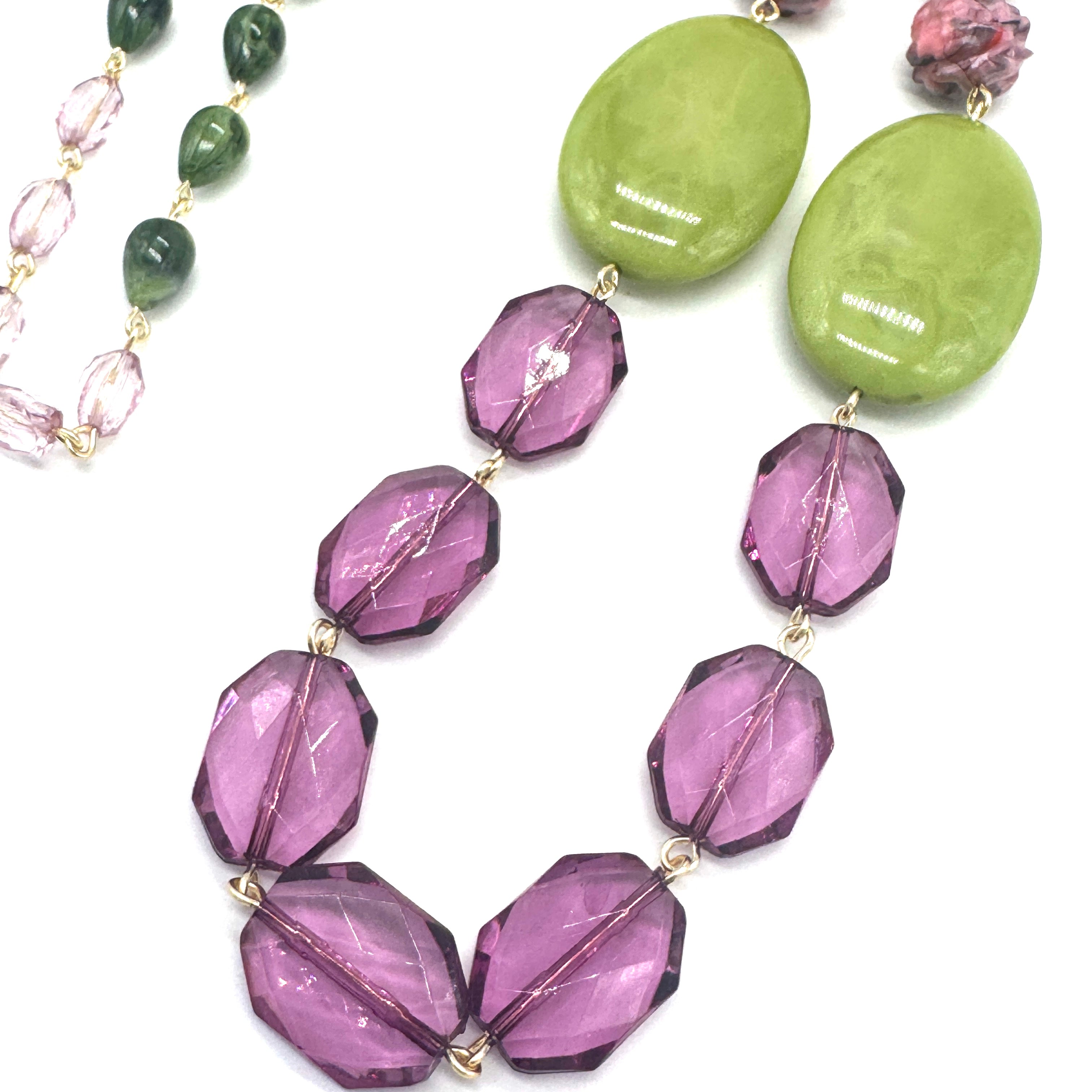 Necklace with purple beads and green stones on a white background