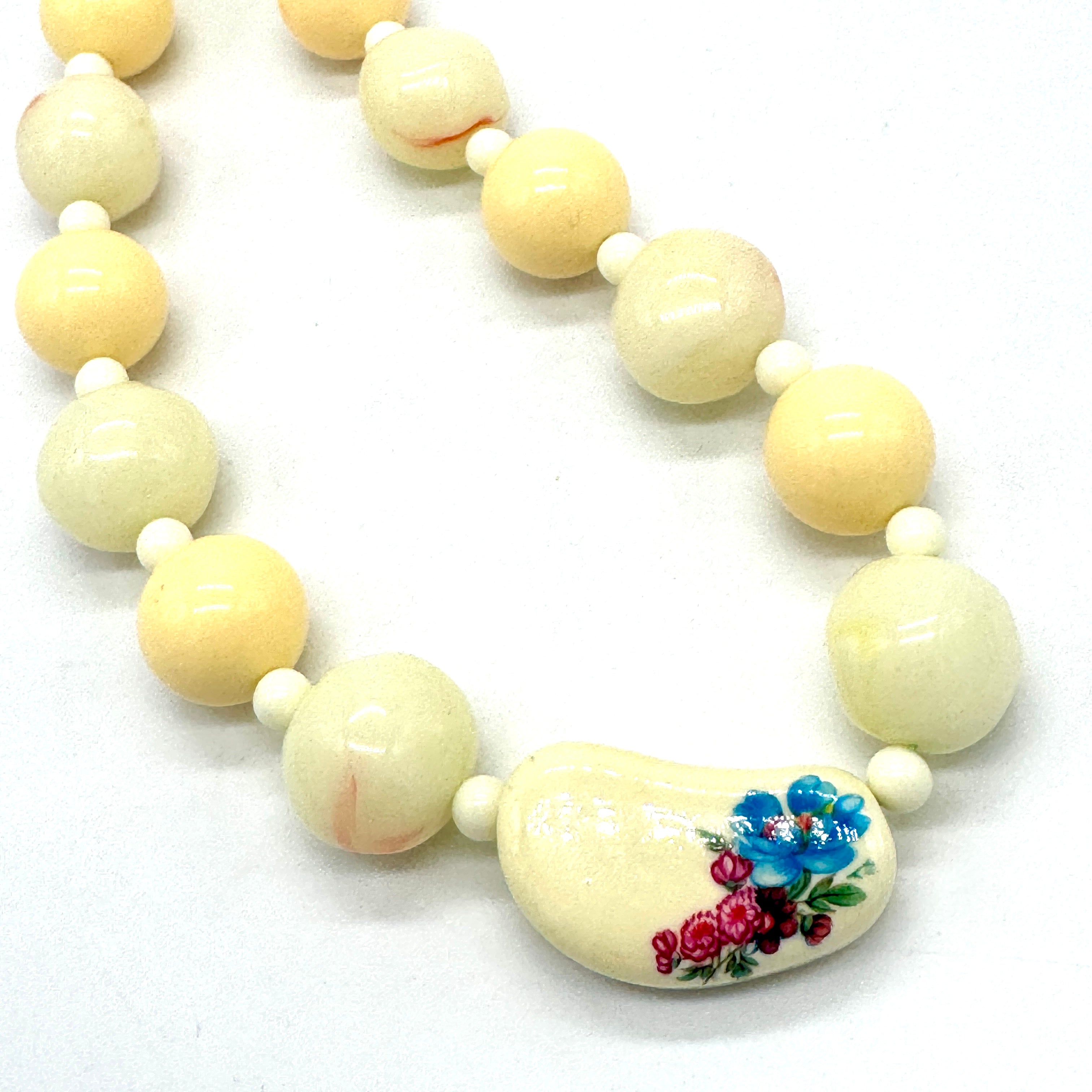 Necklace with cream-colored beads, including a floral pendant on a white background