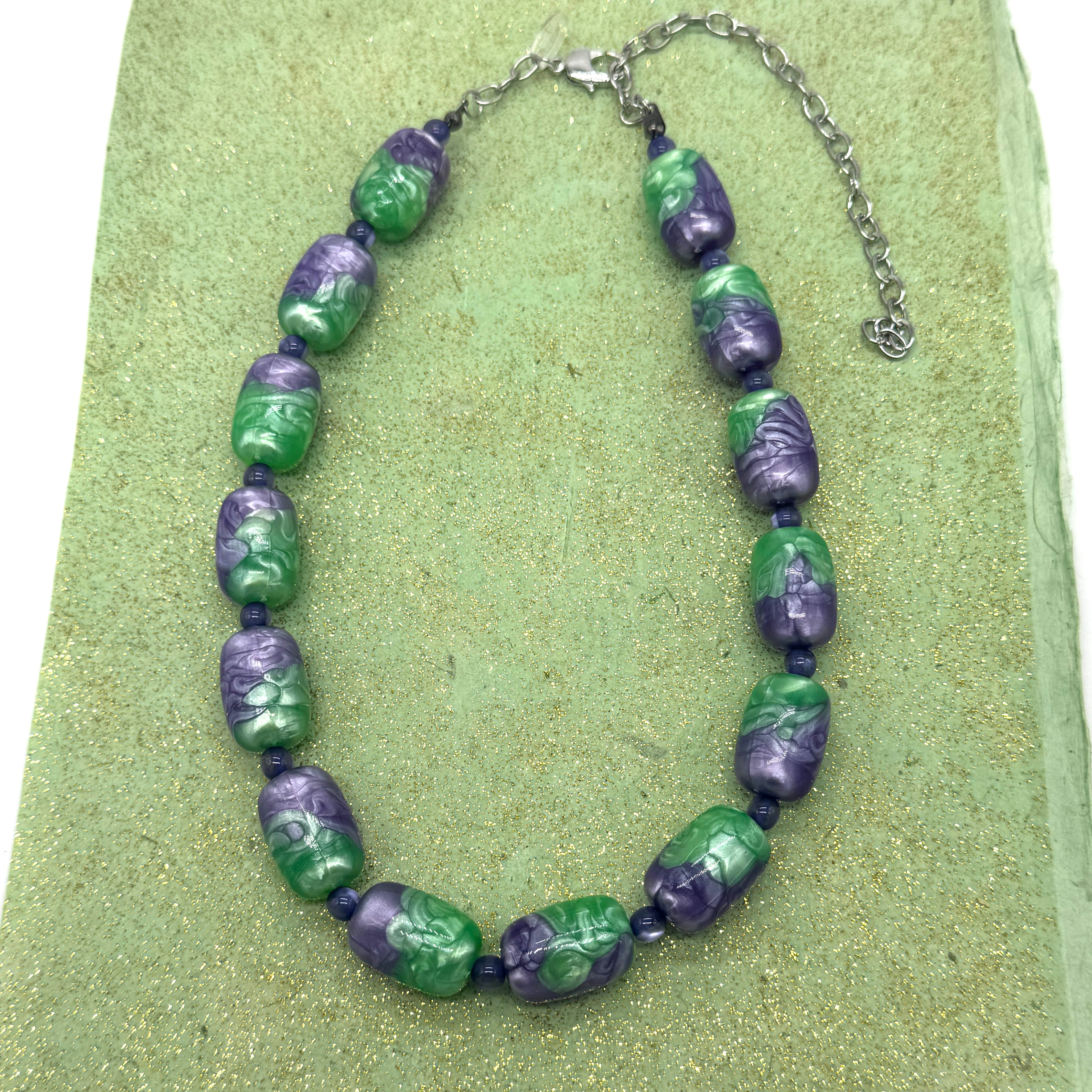 Necklace with green and purple beads on a green textured surface