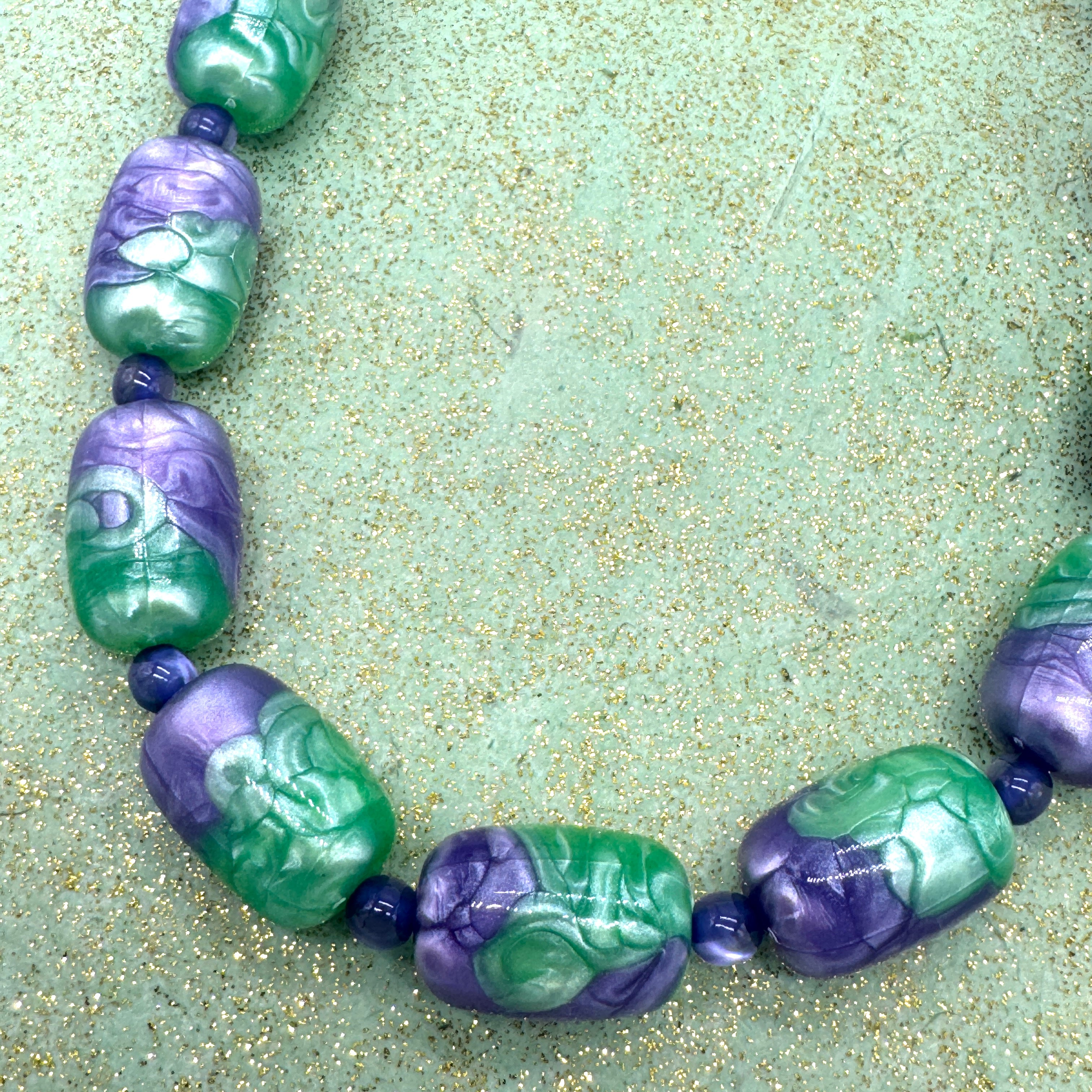 Necklace with green and purple beads on a textured green surface