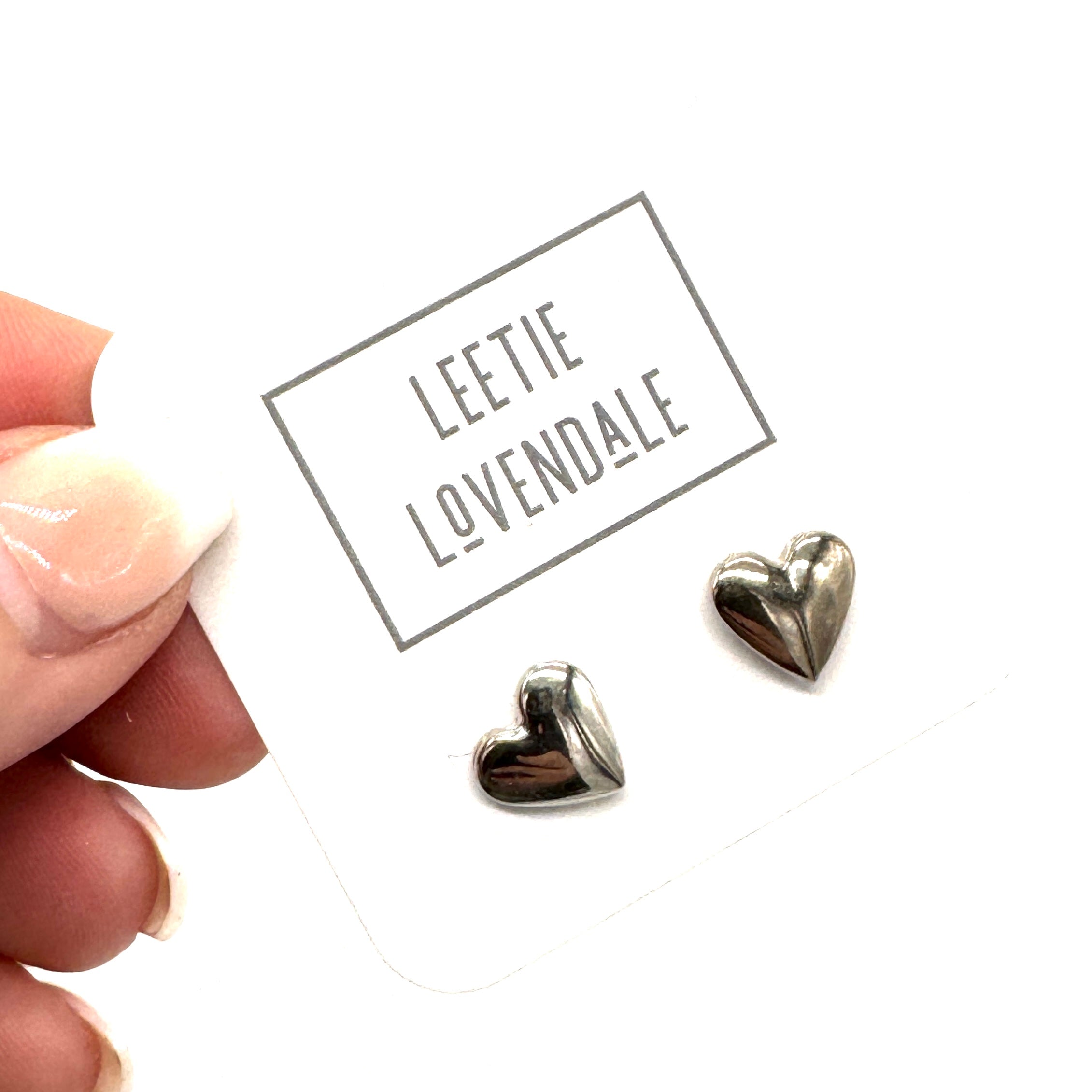 Heart-shaped silver earrings on a white card with &