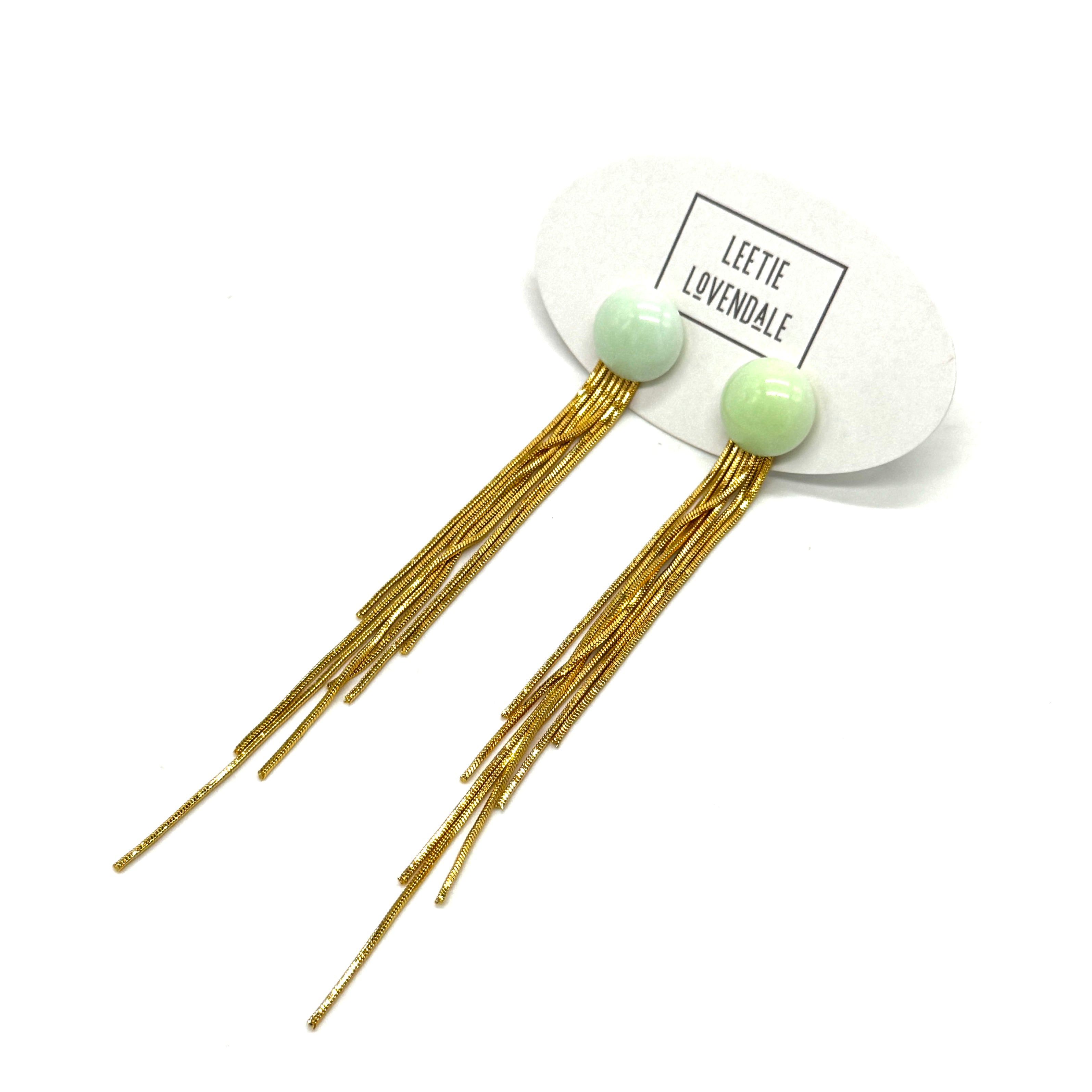Gold fringe earrings with green beads on a white background