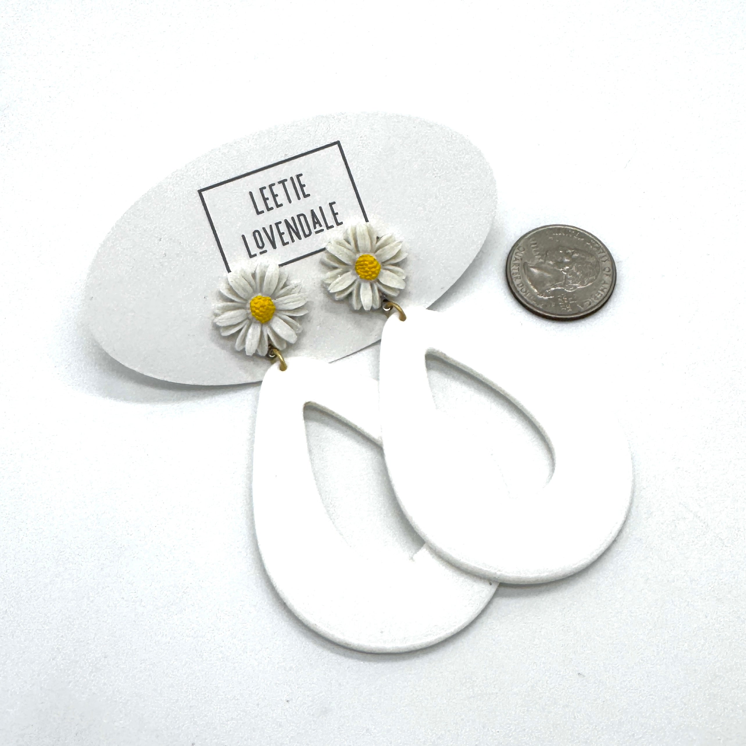 White hoop earrings with daisy flower charms on a white background with &