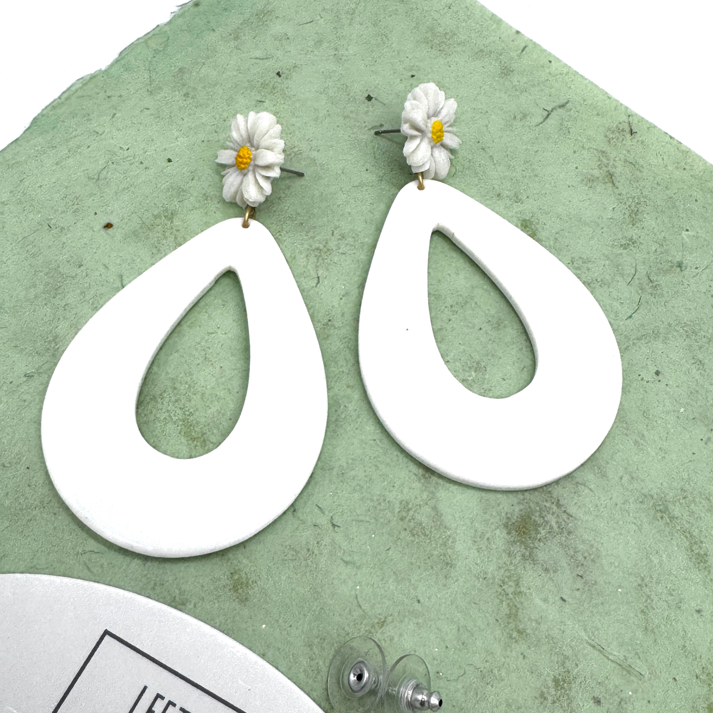 White teardrop earrings with floral tops on a green textured background
