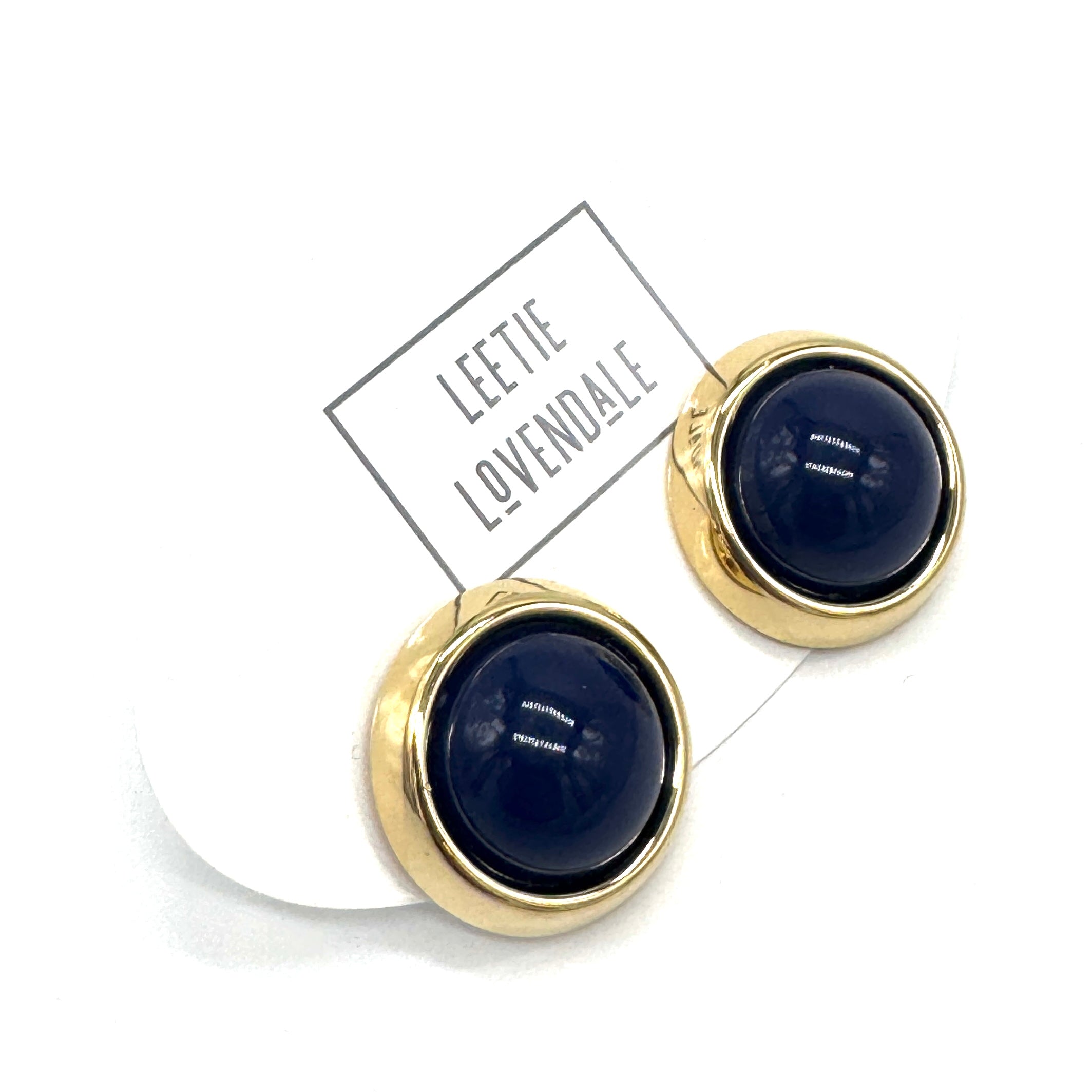 Gold-framed round earrings with dark blue centers on a white background, featuring the brand &