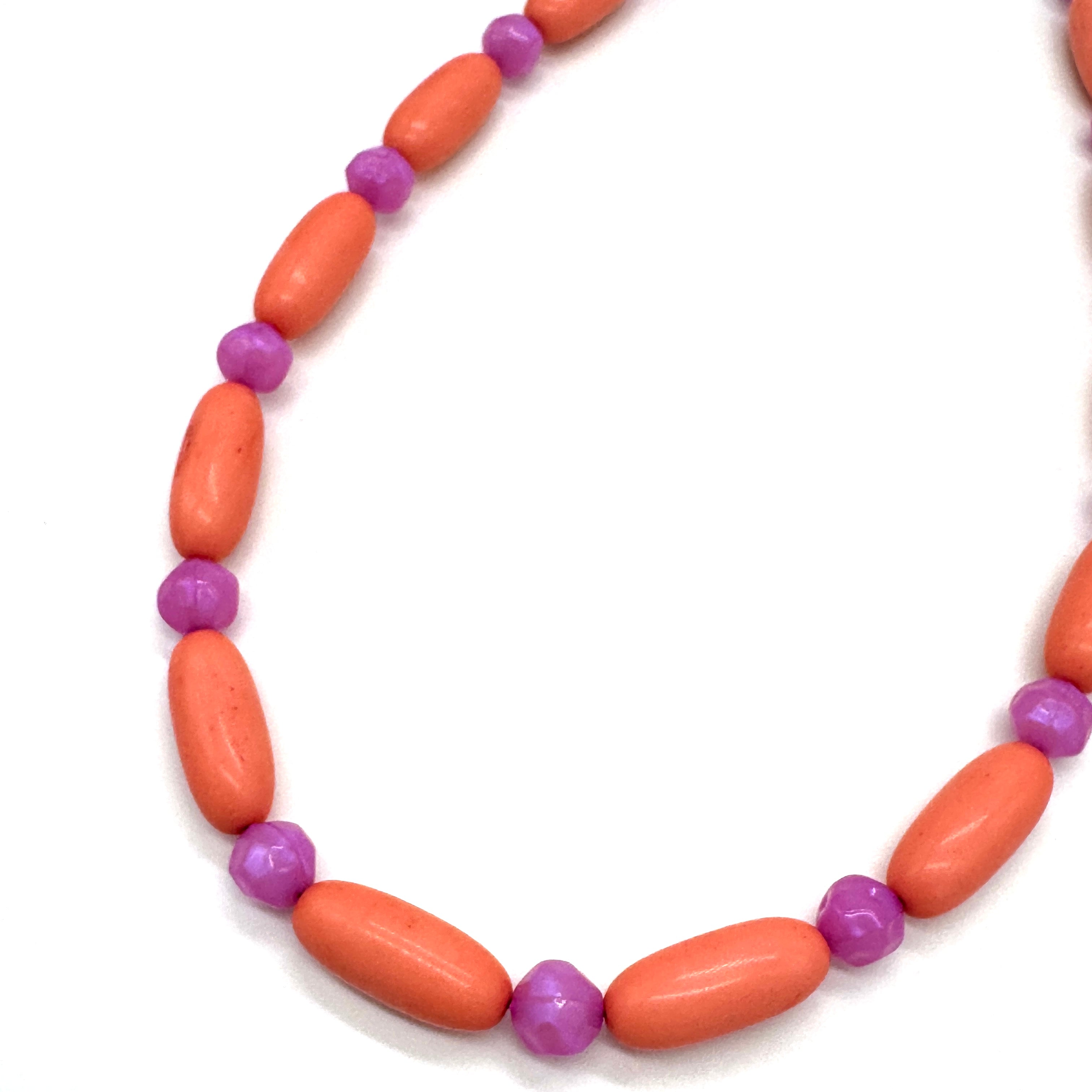 Close up of bright coral and pink beaded necklace on a white background.
