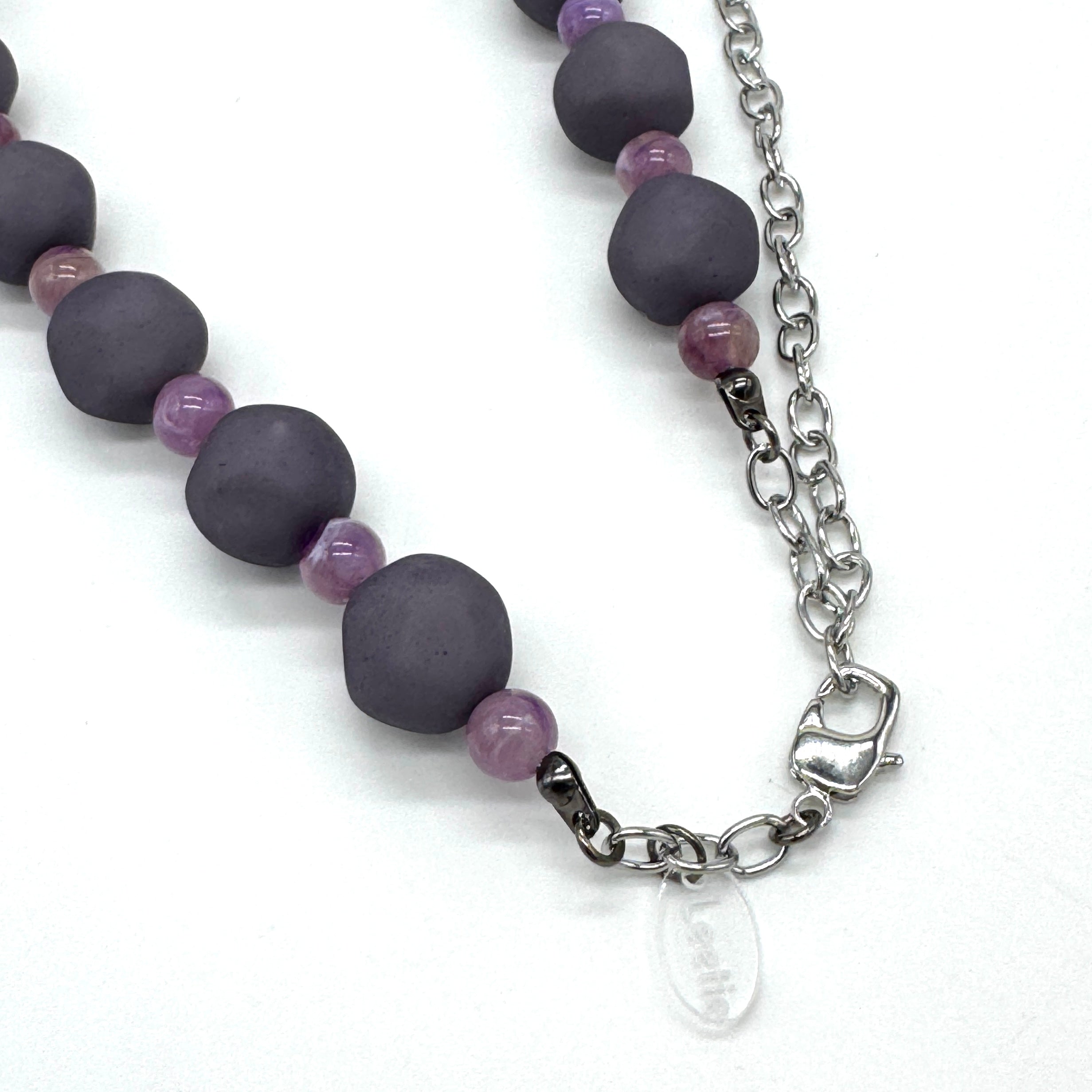 Closeup of adjustable necklace featuring dark gray and lilac lucite beads laid on a white background.