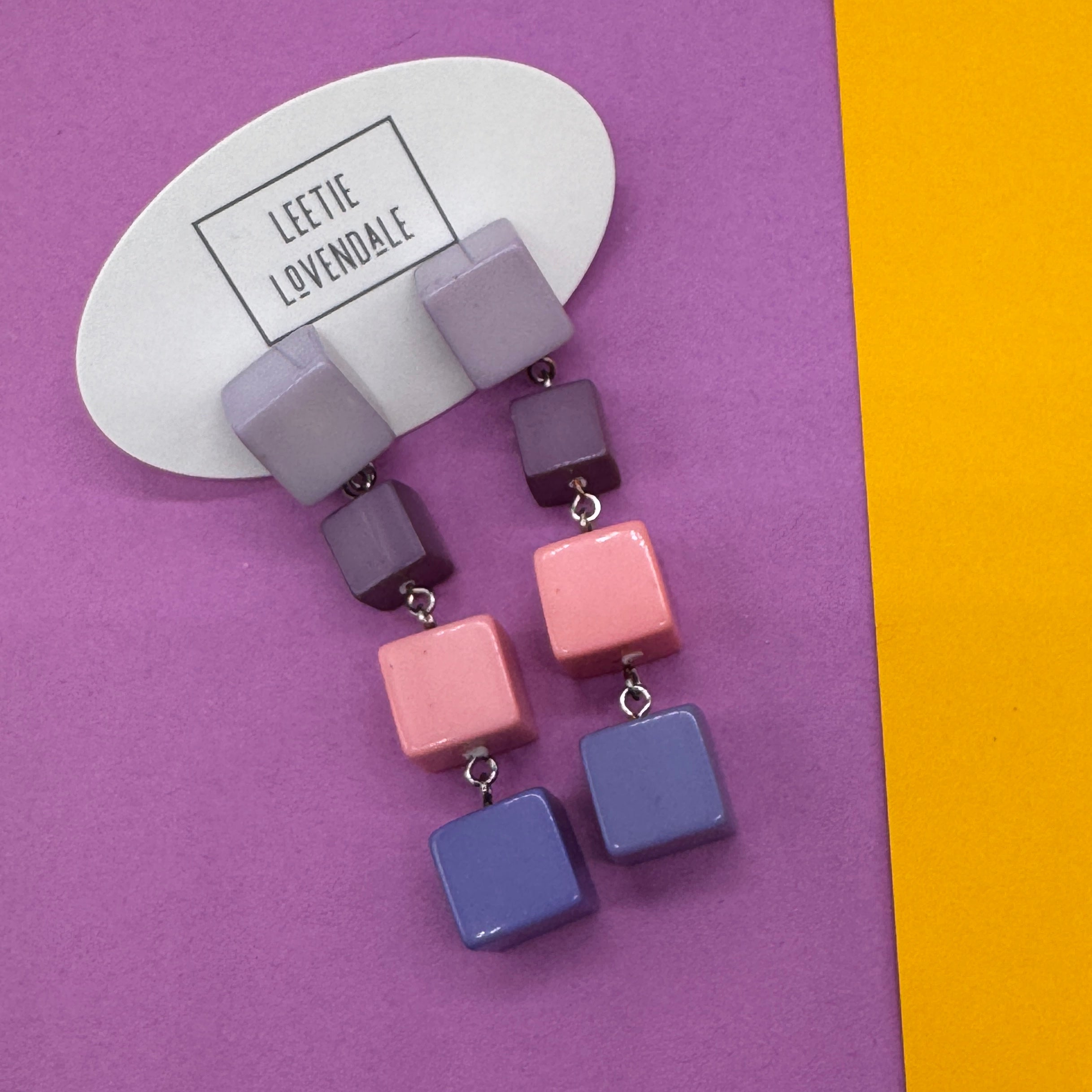 Colorful square earrings on a purple and yellow background with &