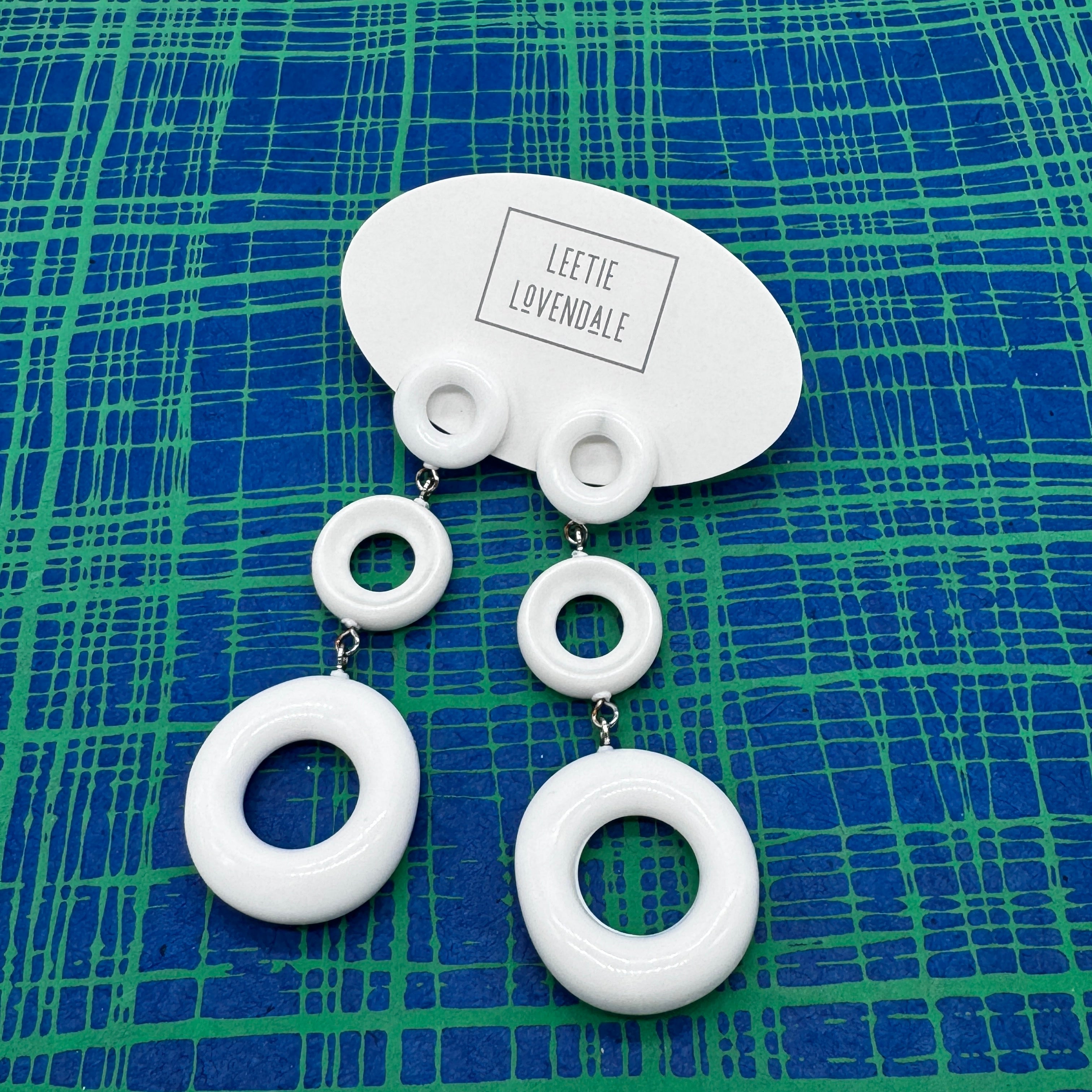 White circular earrings on a blue and green patterned background