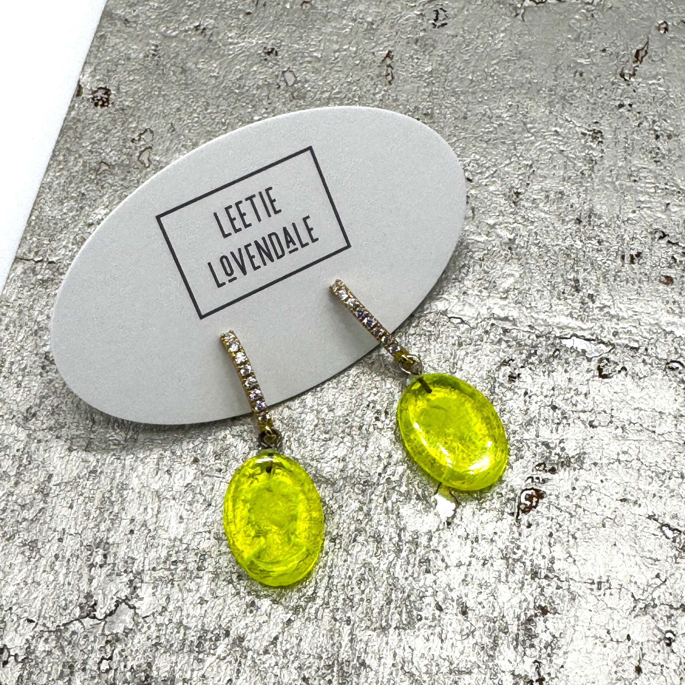 Yellow earrings on a branded card with a textured surface background