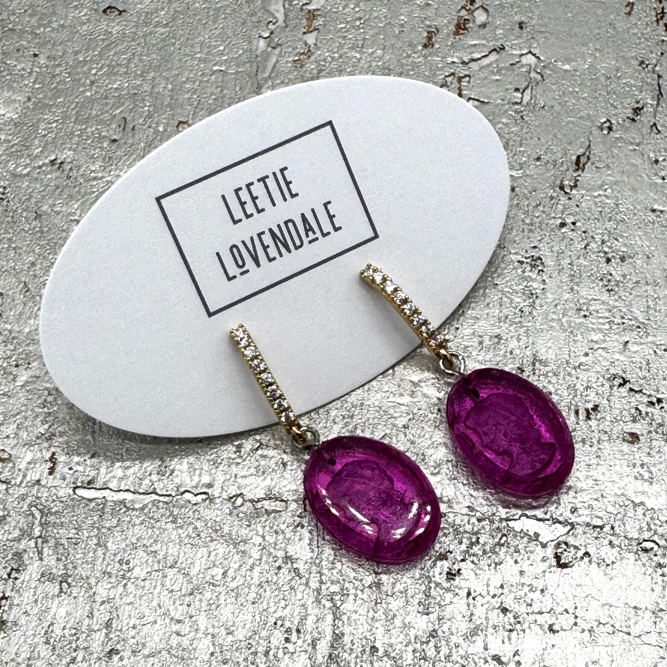 Purple earrings on a branded card with &