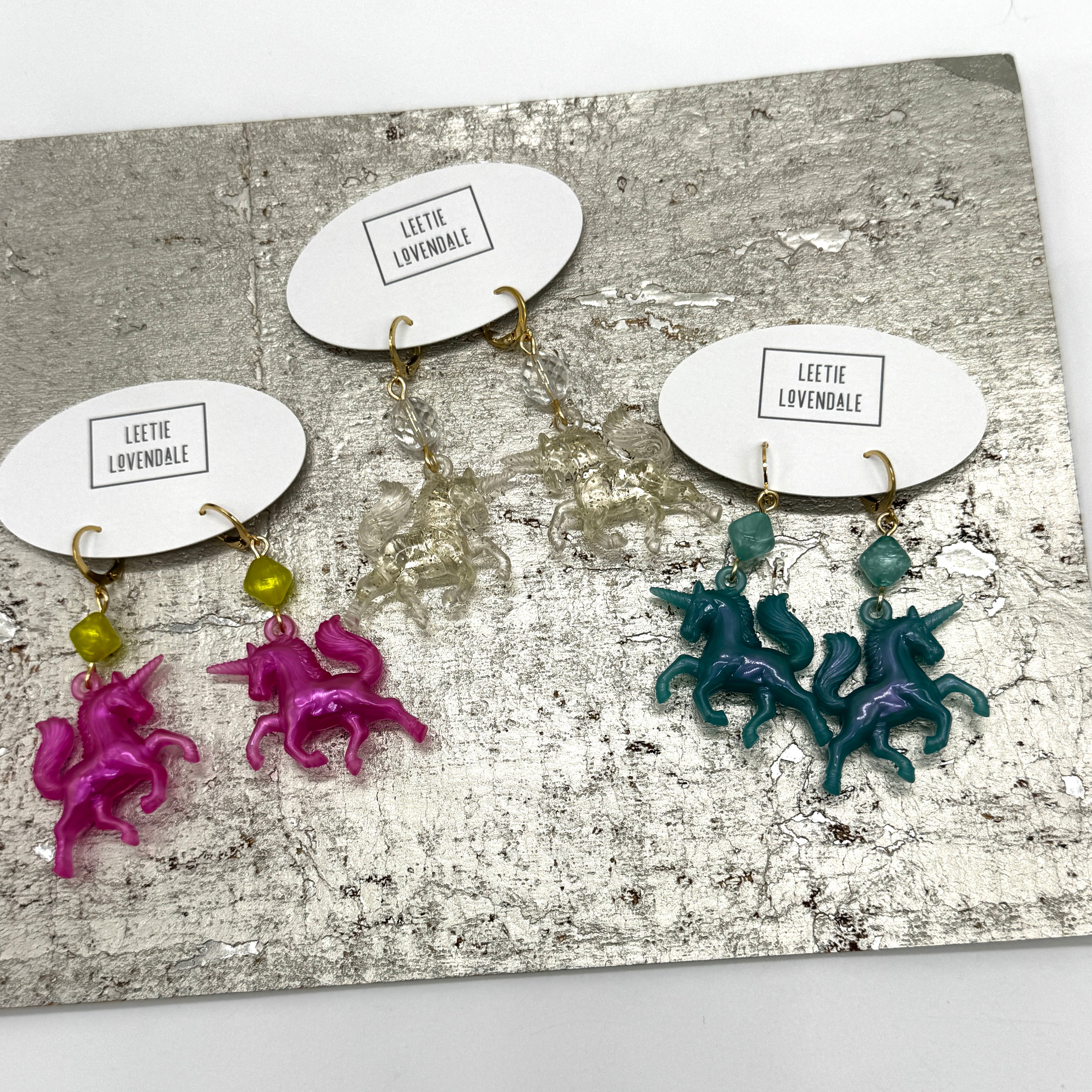 Unicorn-shaped earrings on display with name tags on a textured surface