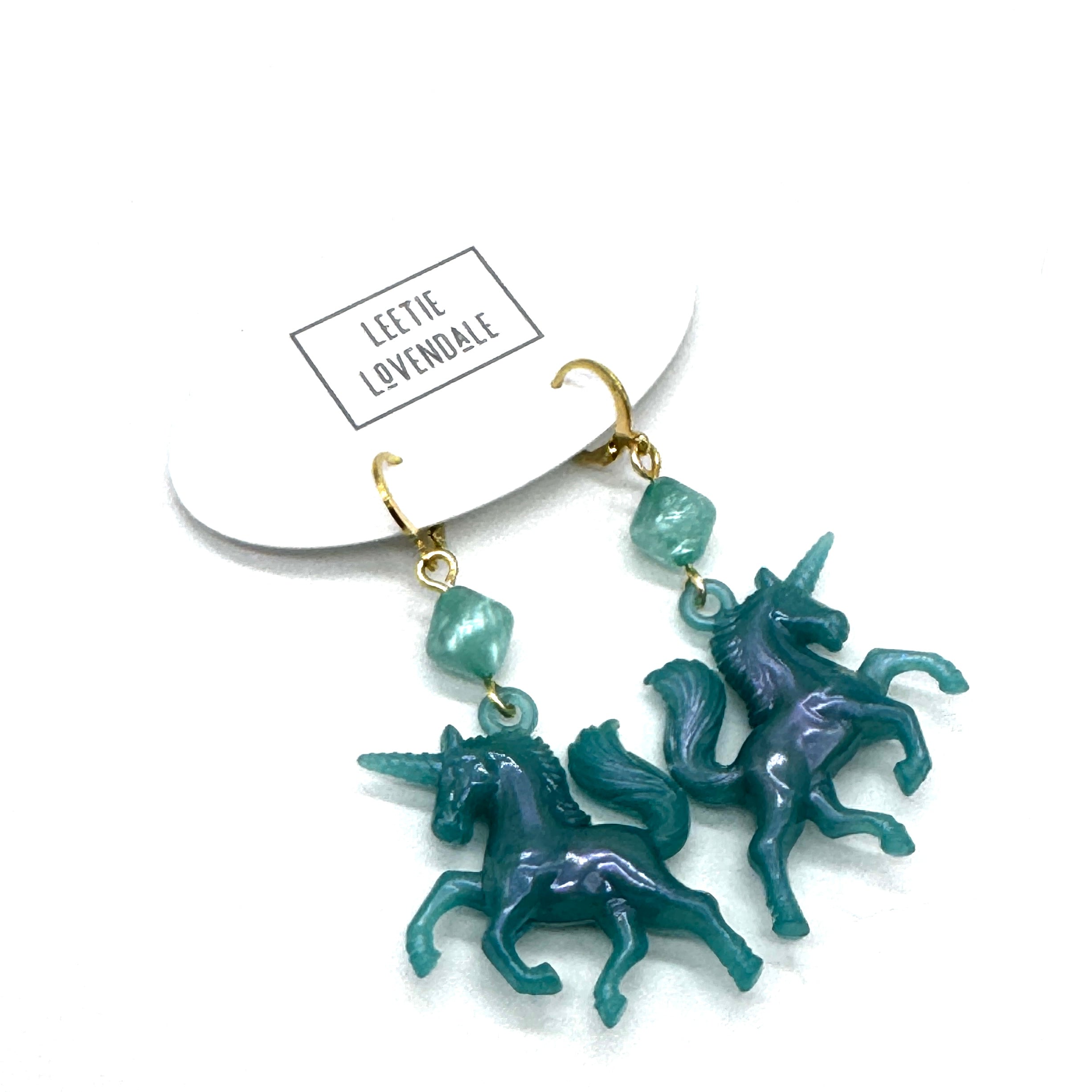 Teal unicorn earrings with gold hooks on a white background, featuring the brand &