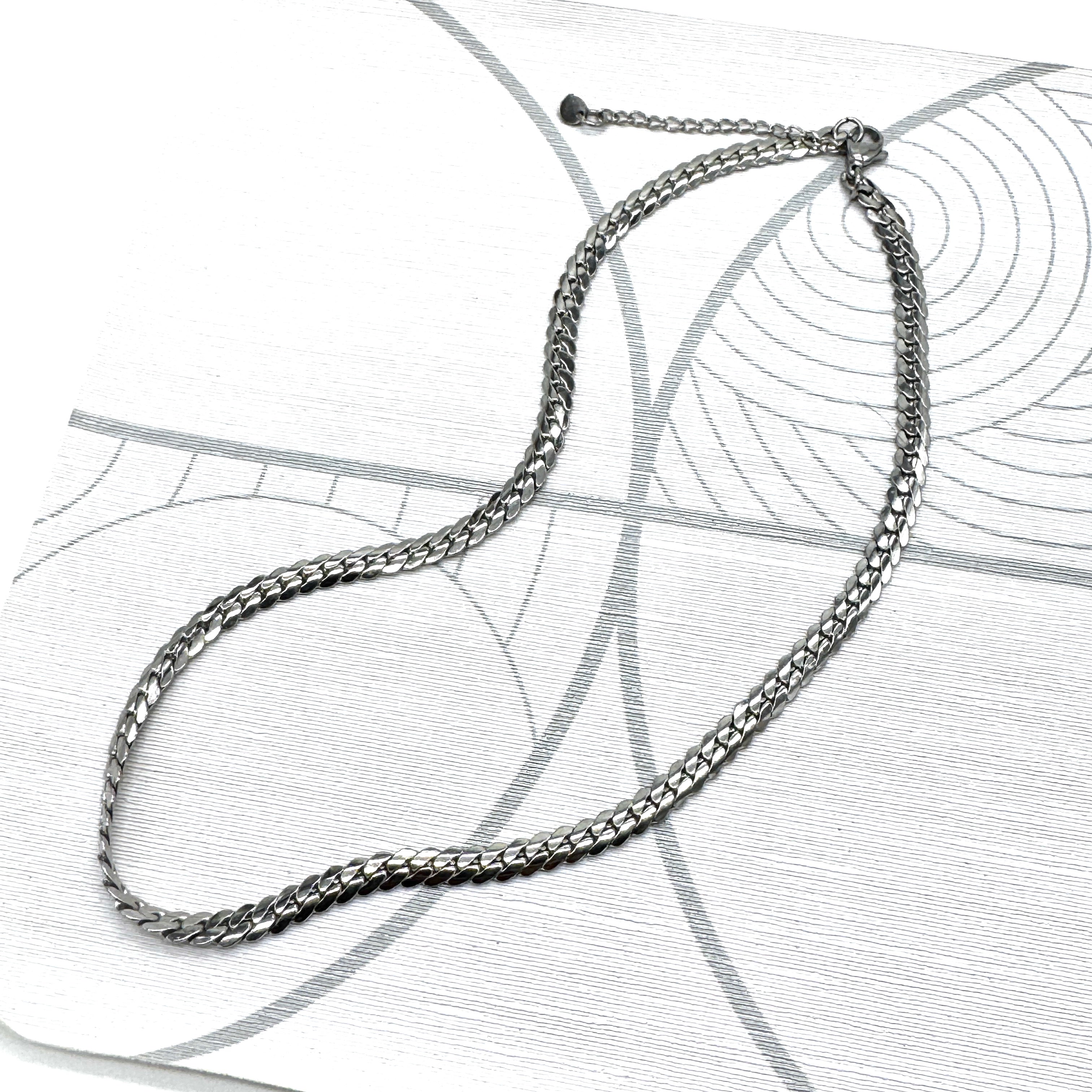Adjustable silver snake chain necklace on a patterned background.