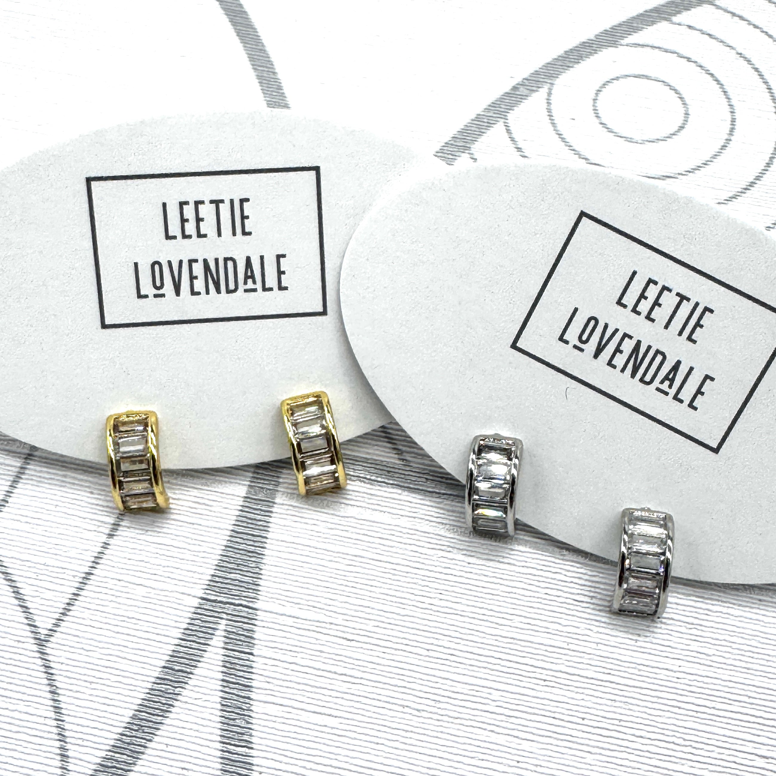 Silver and gold crystal hoop earrings on branded earring cards.