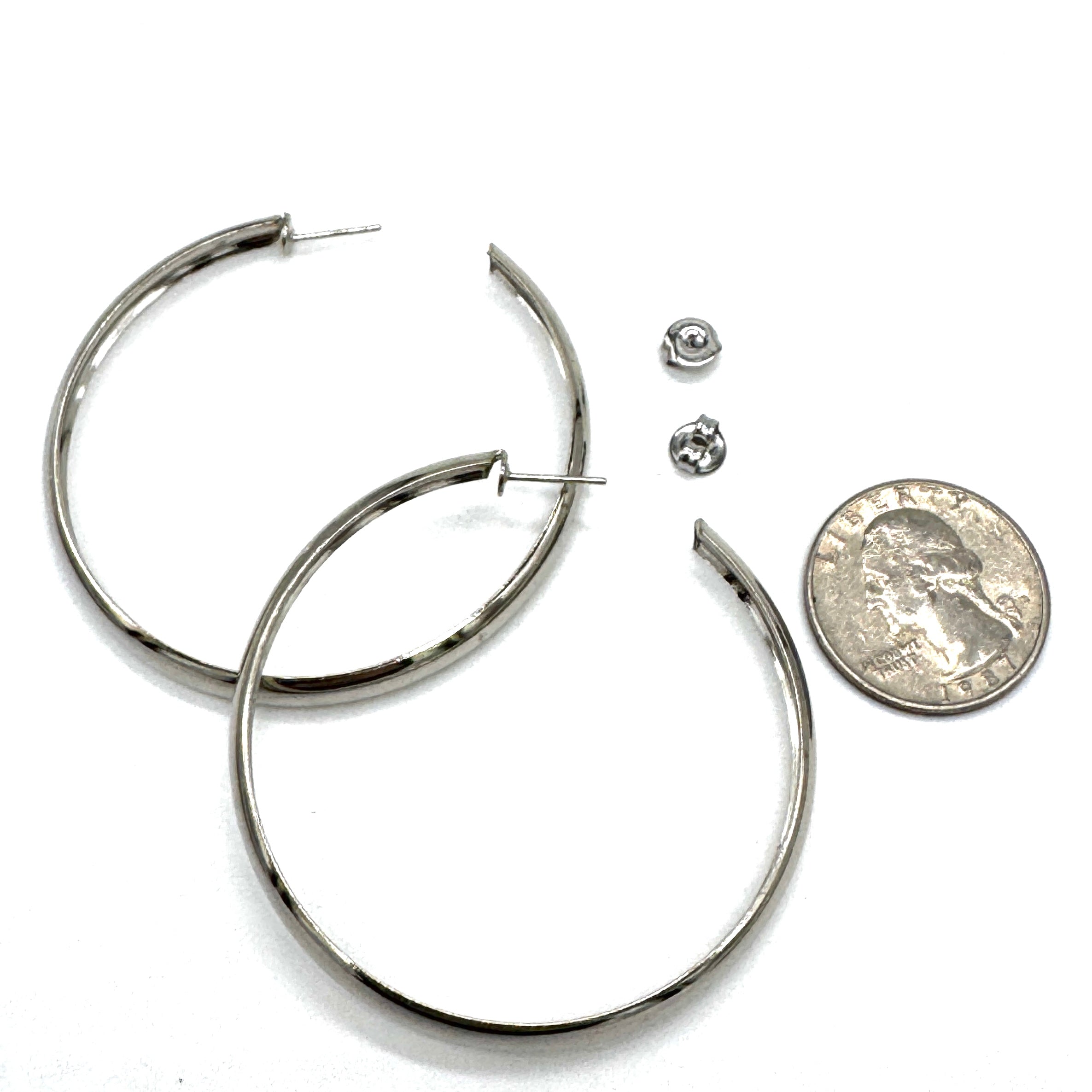 Large silver hoop earrings on a white background with a quarter for scale.