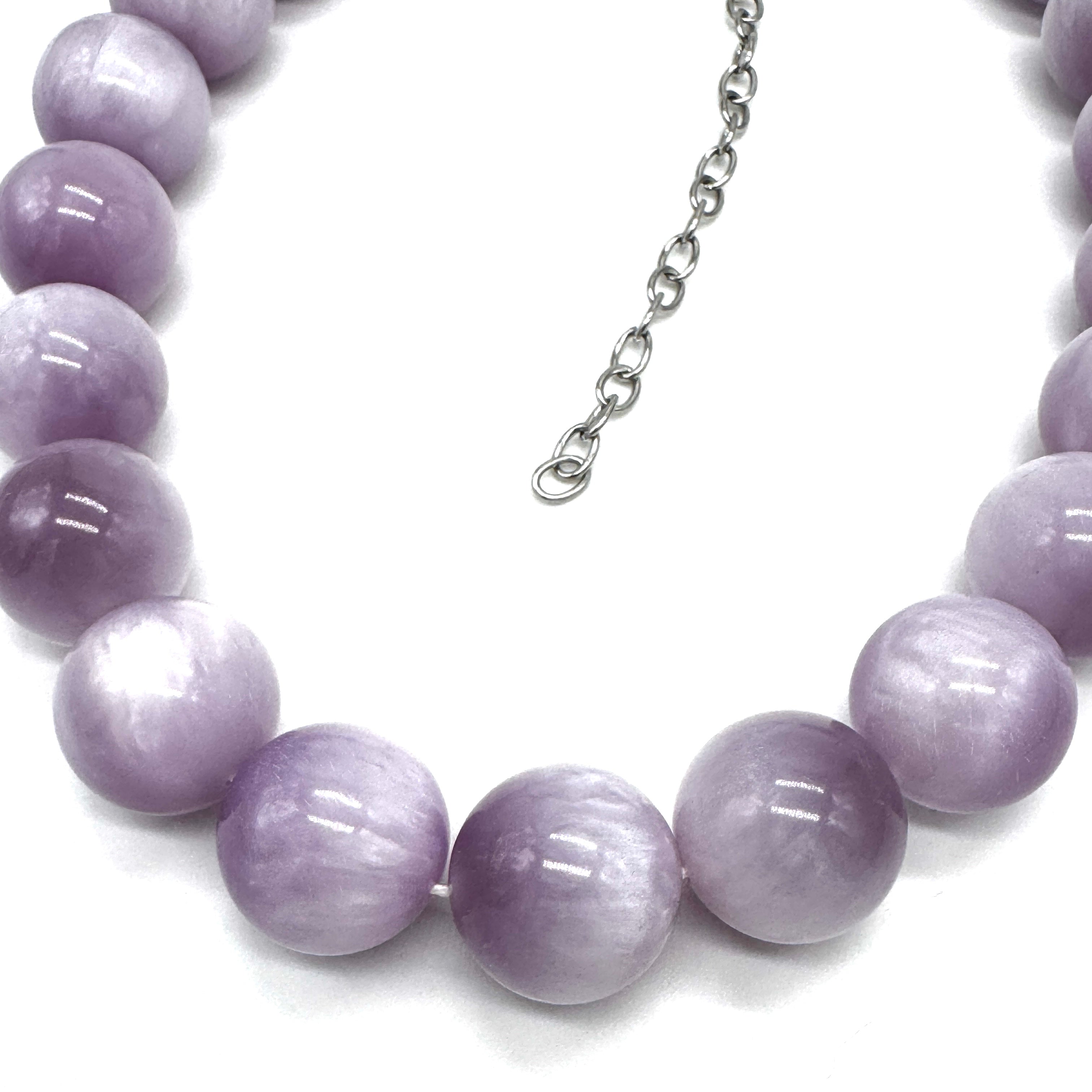 A close-up of a beaded necklace made of large, smooth lavender-purple oval beads with a silver-tone chain extender, shown on a plain white background.