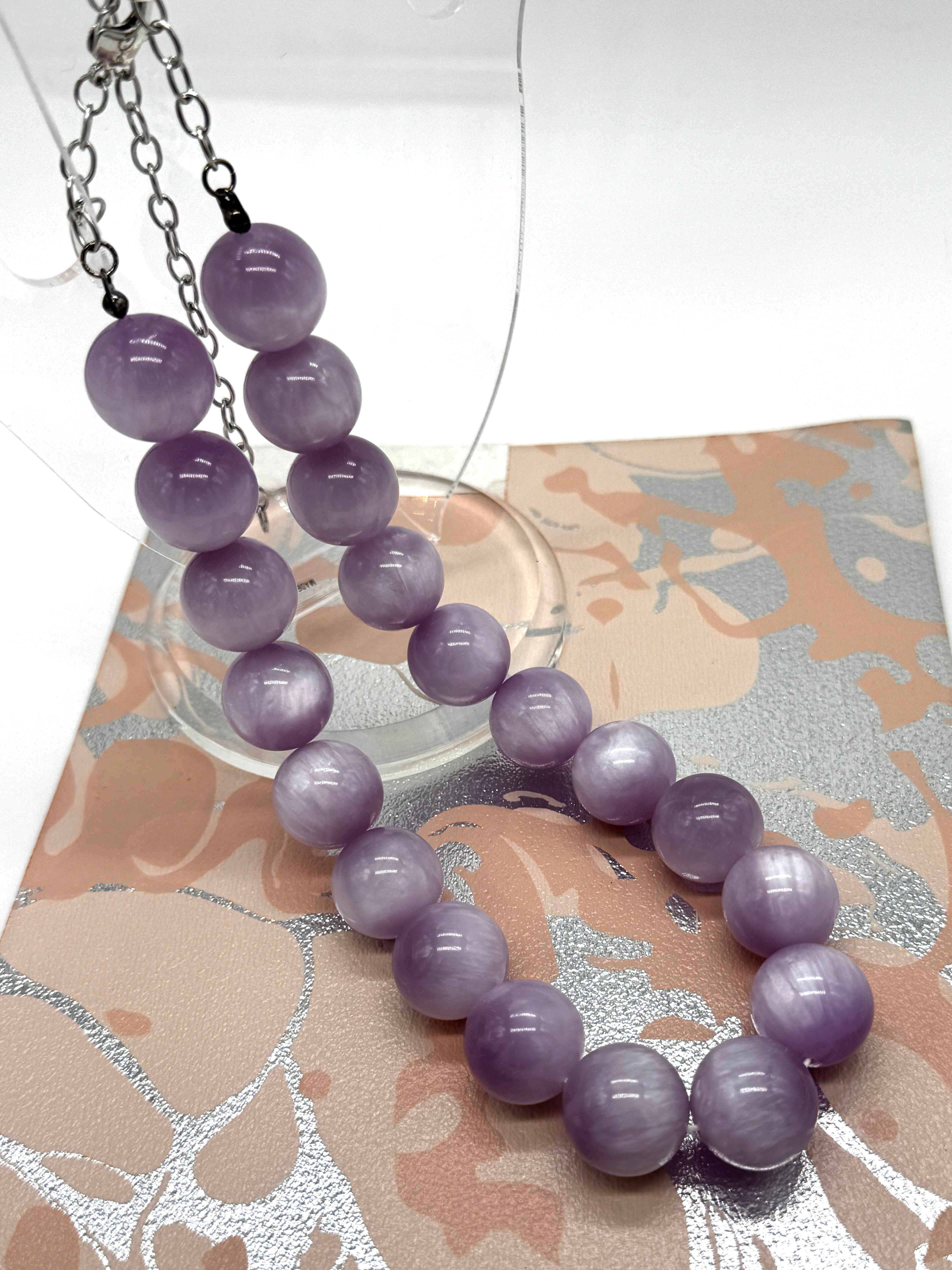 A purple bead necklaces with silver chains, displayed on a decorative patterned card.
