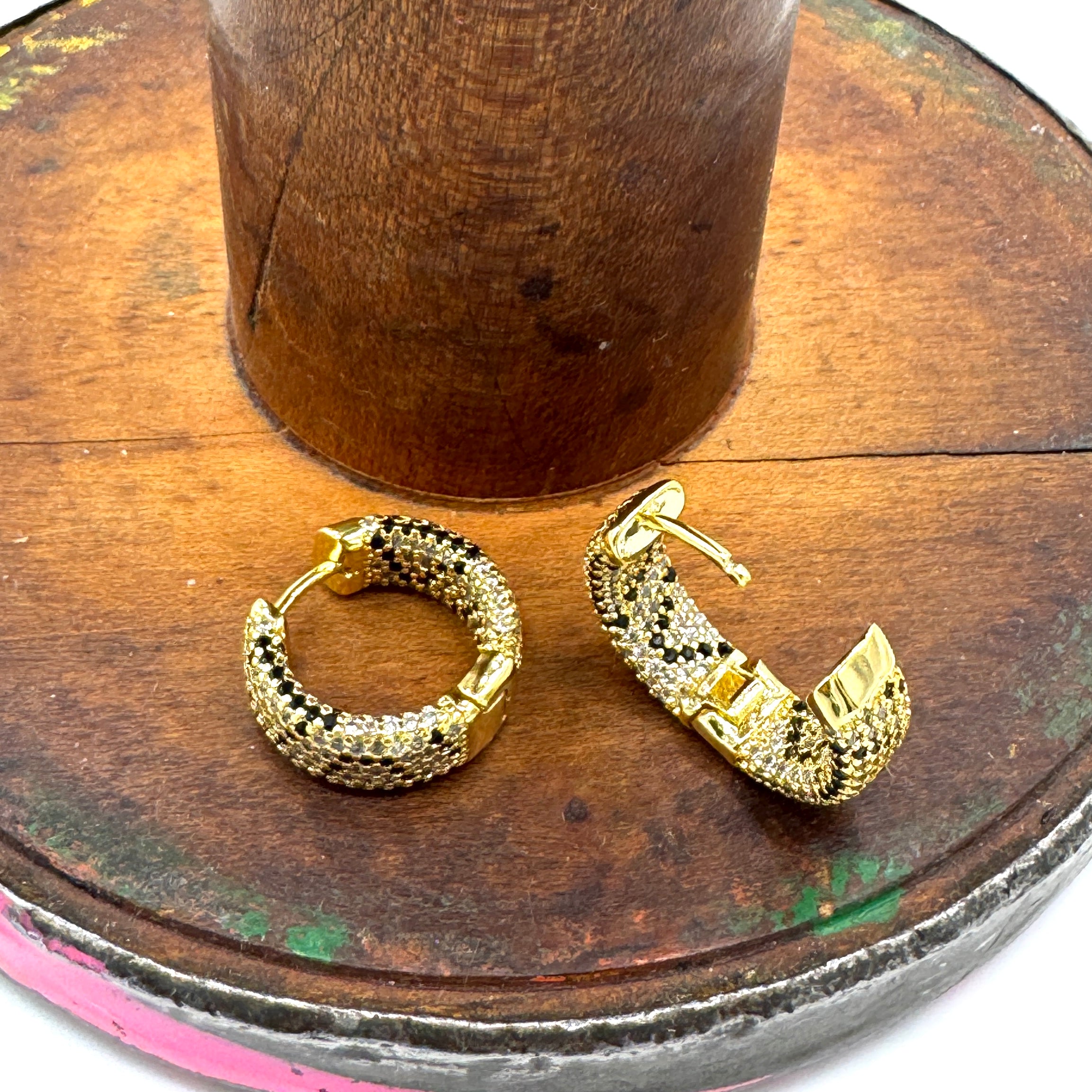 A pair of gold hoop earrings with a textured rhinestone pattern, displayed on a rustic wooden surface.