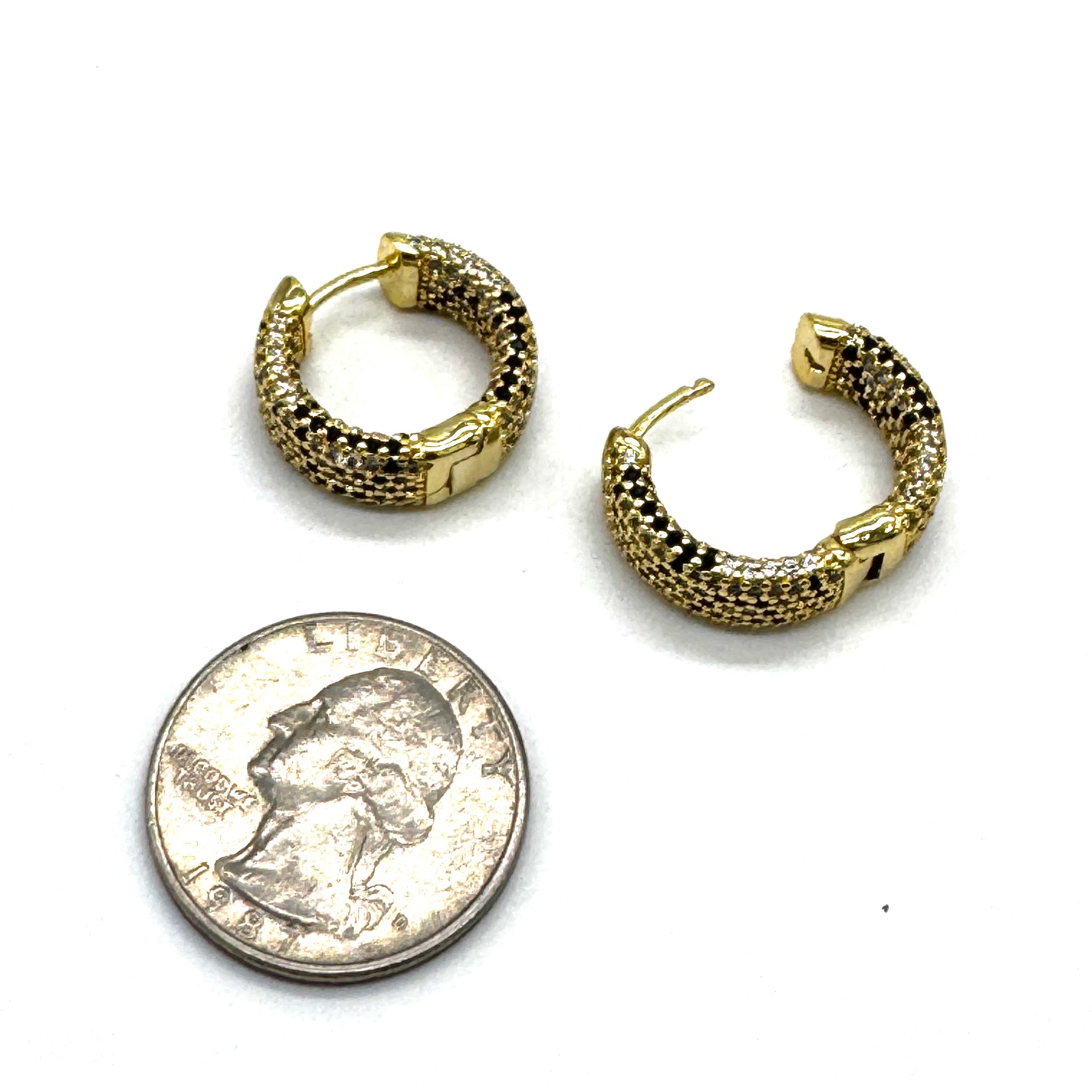 A pair of small gold hoop earrings with a textured pave finish, displayed next to a US quarter coin for scale on a white background.