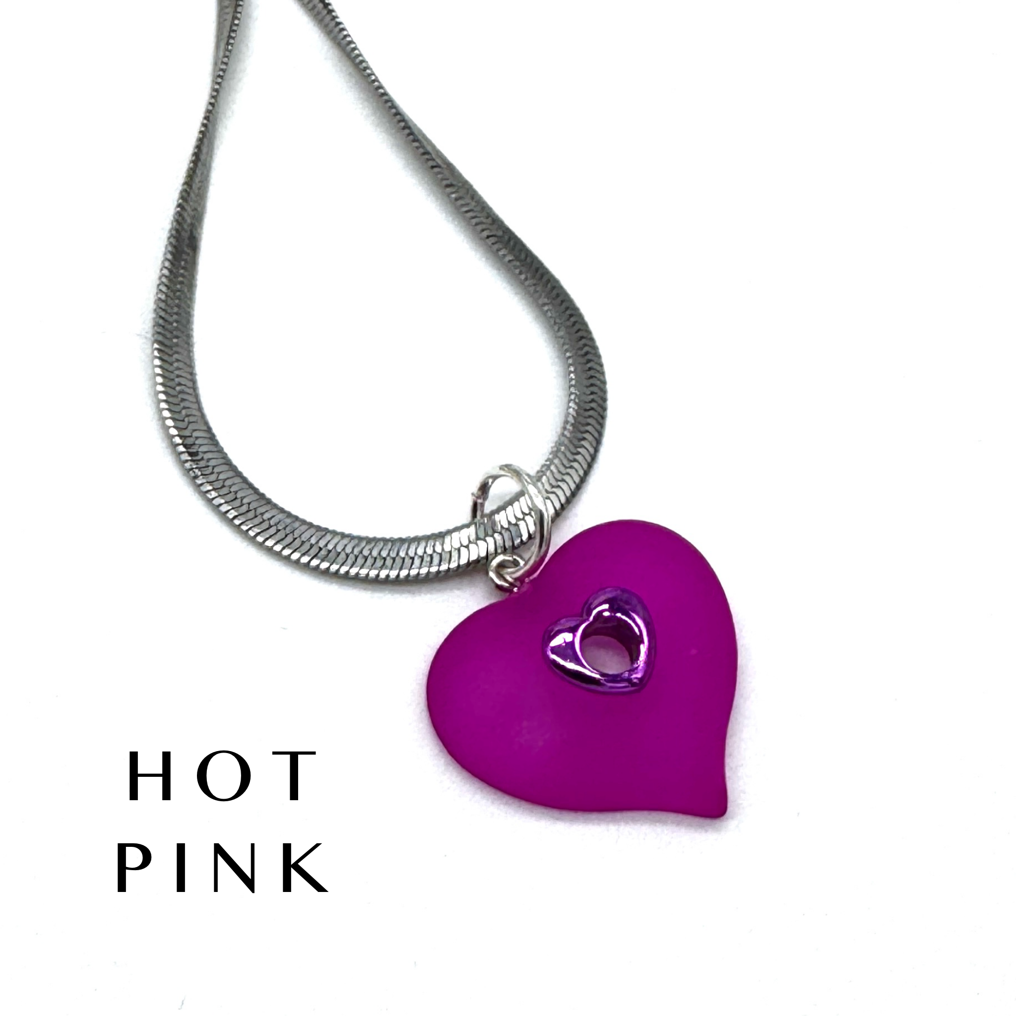 A silver snake chain necklace with a hot pink heart-shaped pendant featuring a smaller silver heart cutout in the center, shown on a white background with the text &