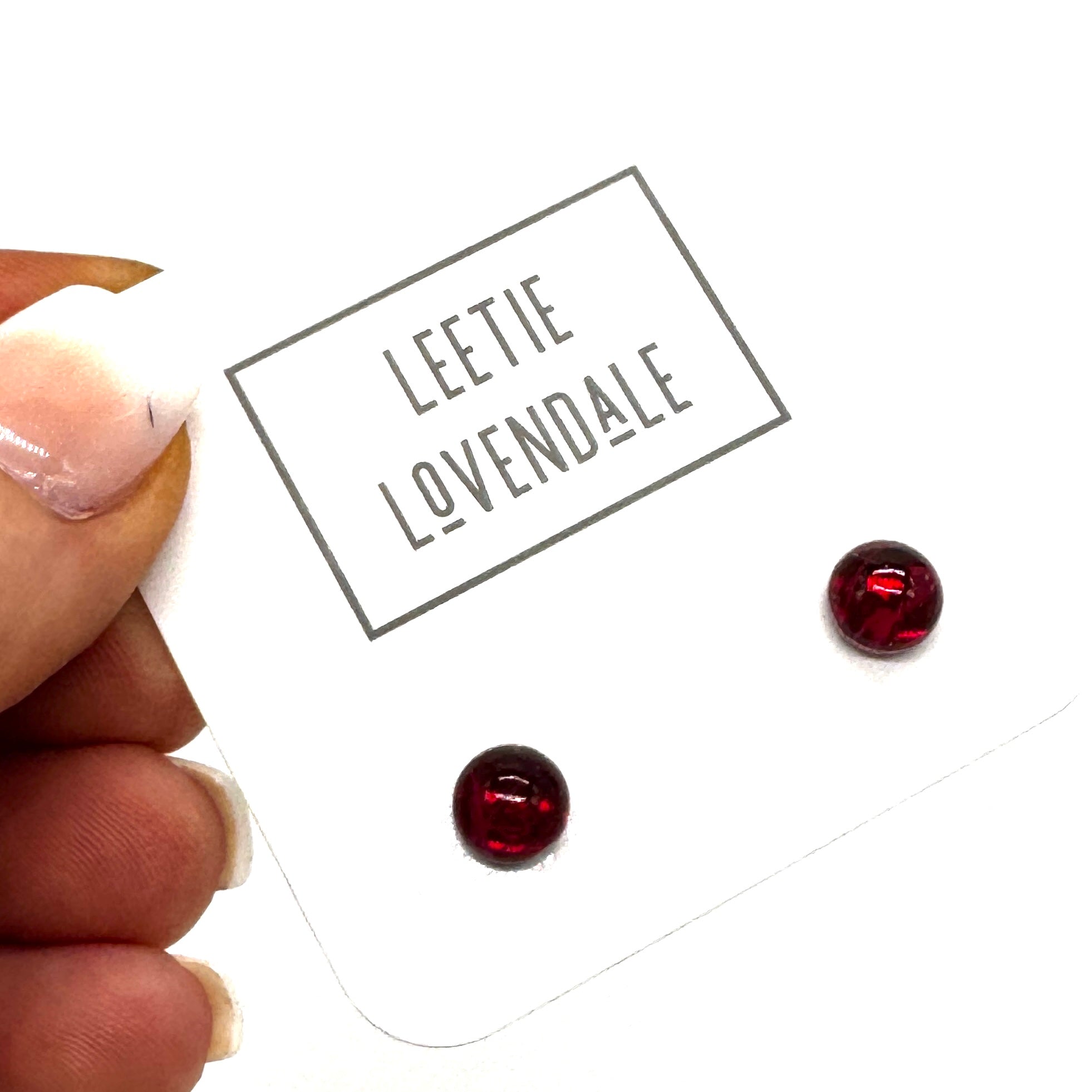A close-up of a hand holding a white display card with the brand name &