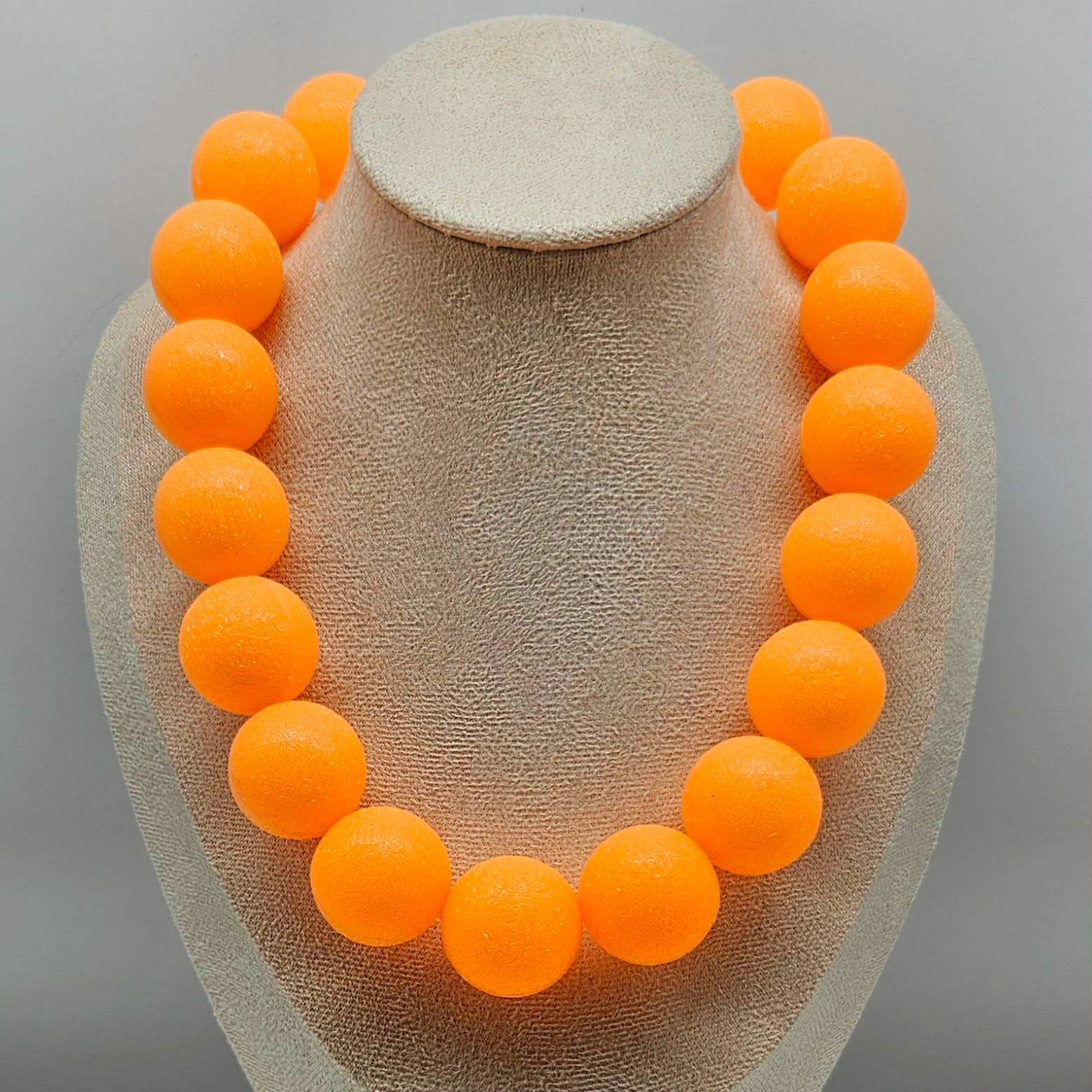 Necklace with orange beads on a gray stand