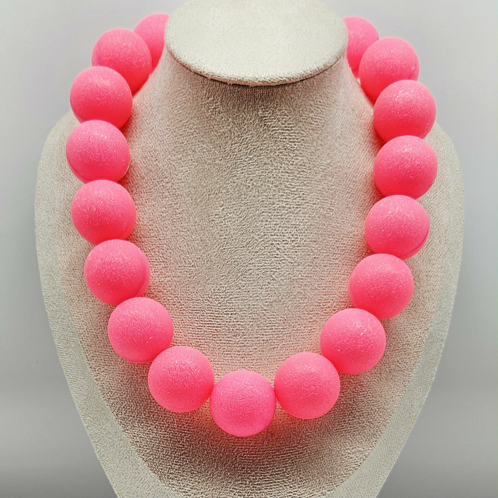 Necklace with pink beads on a beige display stand against a light gray background