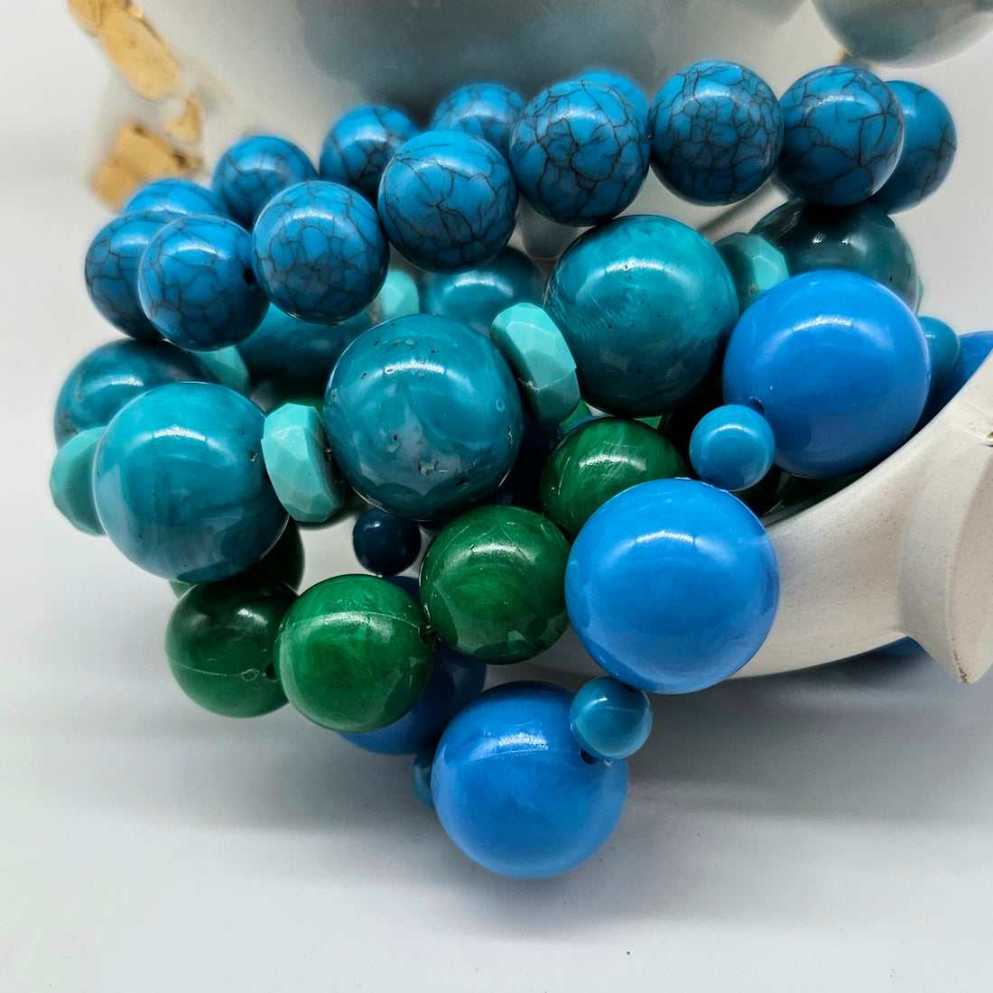 Colorful beaded bracelets with blue, green, and turquoise beads in a white bowl.