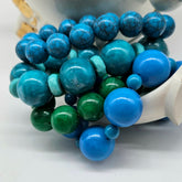 Colorful beaded bracelets with blue, green, and turquoise beads in a white bowl.