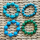 Four beaded bracelets, in blues and one green, on a woven surface.