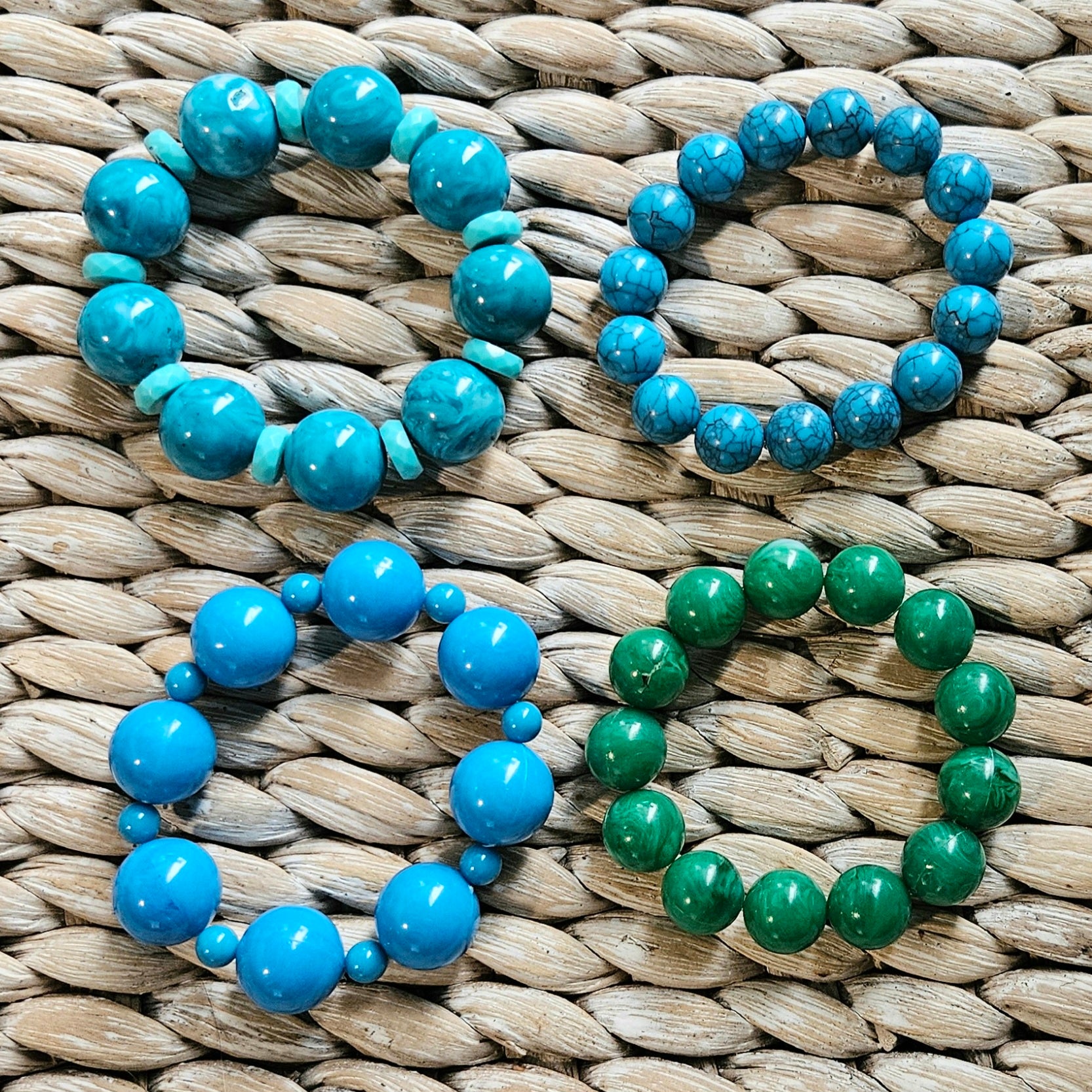 Four beaded bracelets, in blues and one green, on a woven surface.