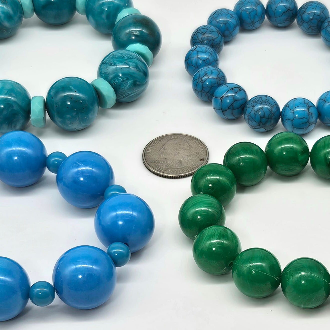 Four nracelets with blue and green beads, one with a coin for size reference, on a white background.