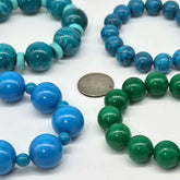 Four nracelets with blue and green beads, one with a coin for size reference, on a white background.