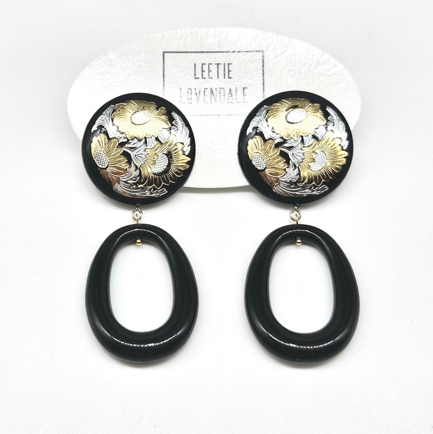 Black and gold floral earrings on a white background with &
