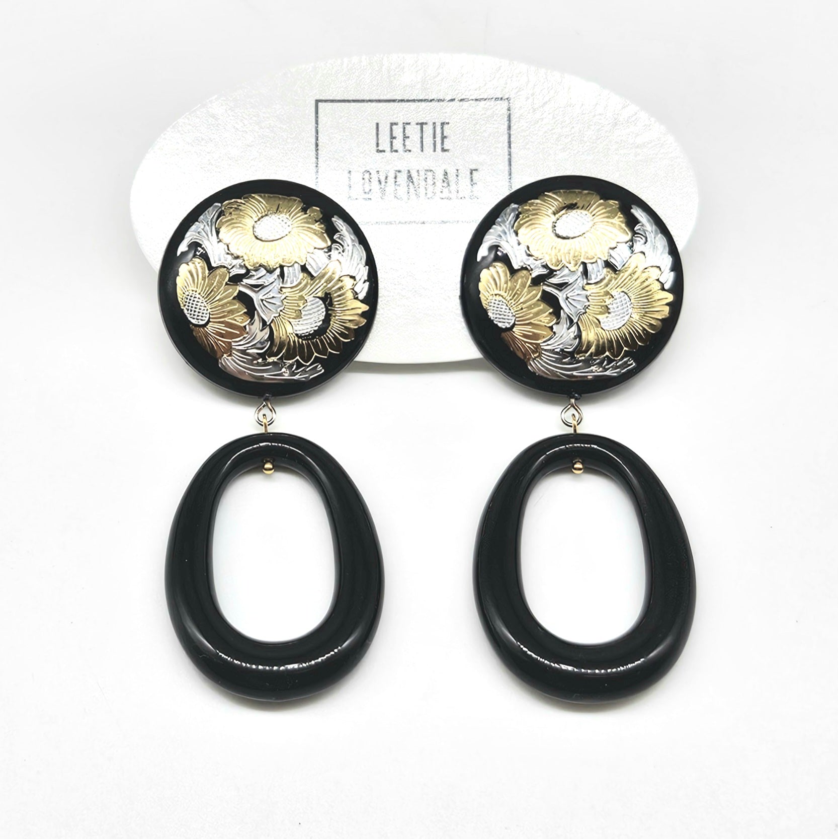 Black and gold floral earrings on a white background with &