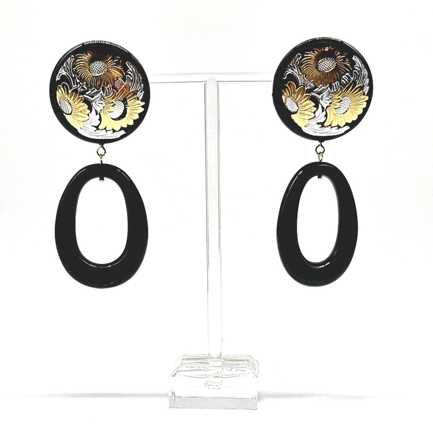 Pair of earrings with floral design and black oval shapes on a clear stand.